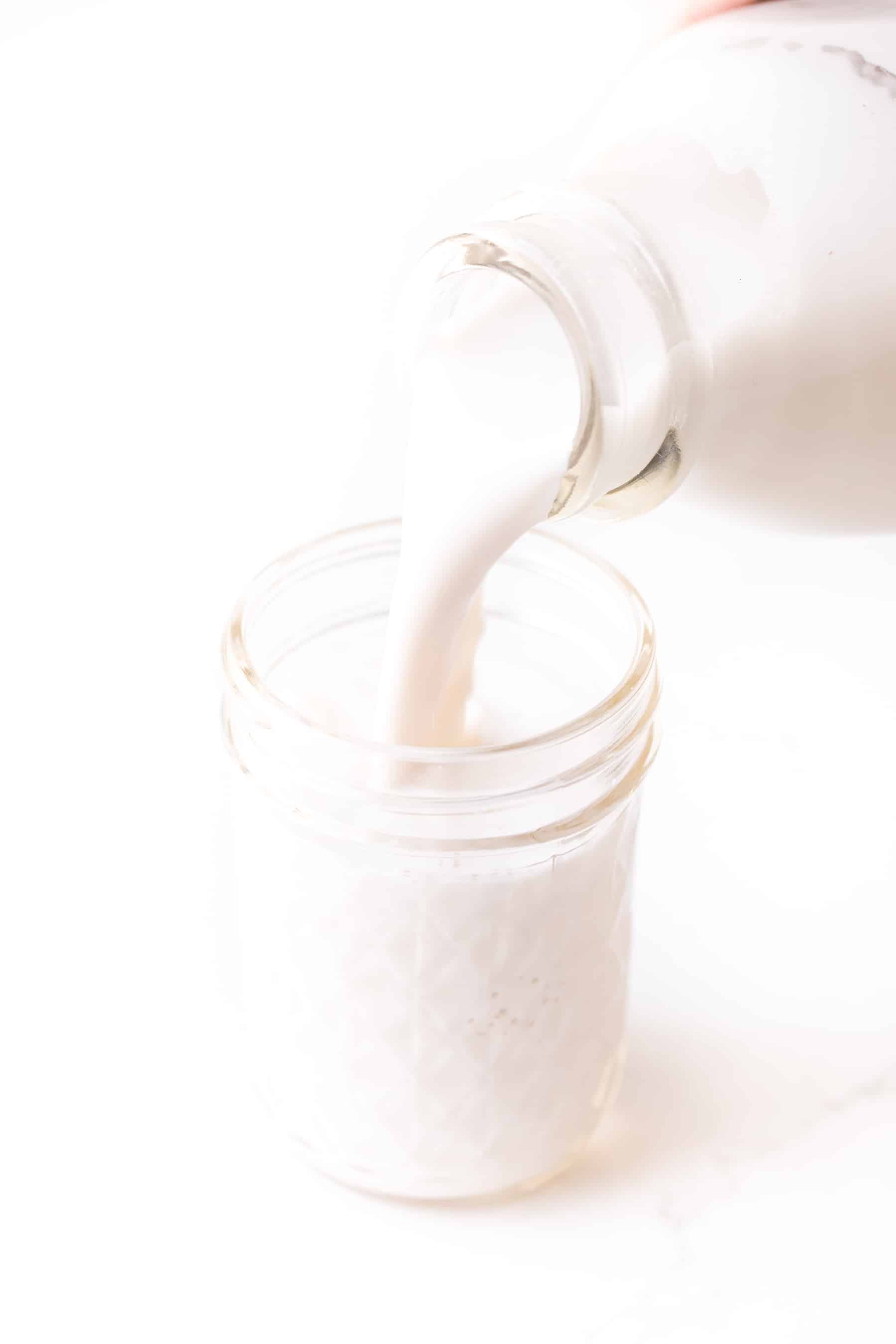 Almond milk being poured into a jar on a white background