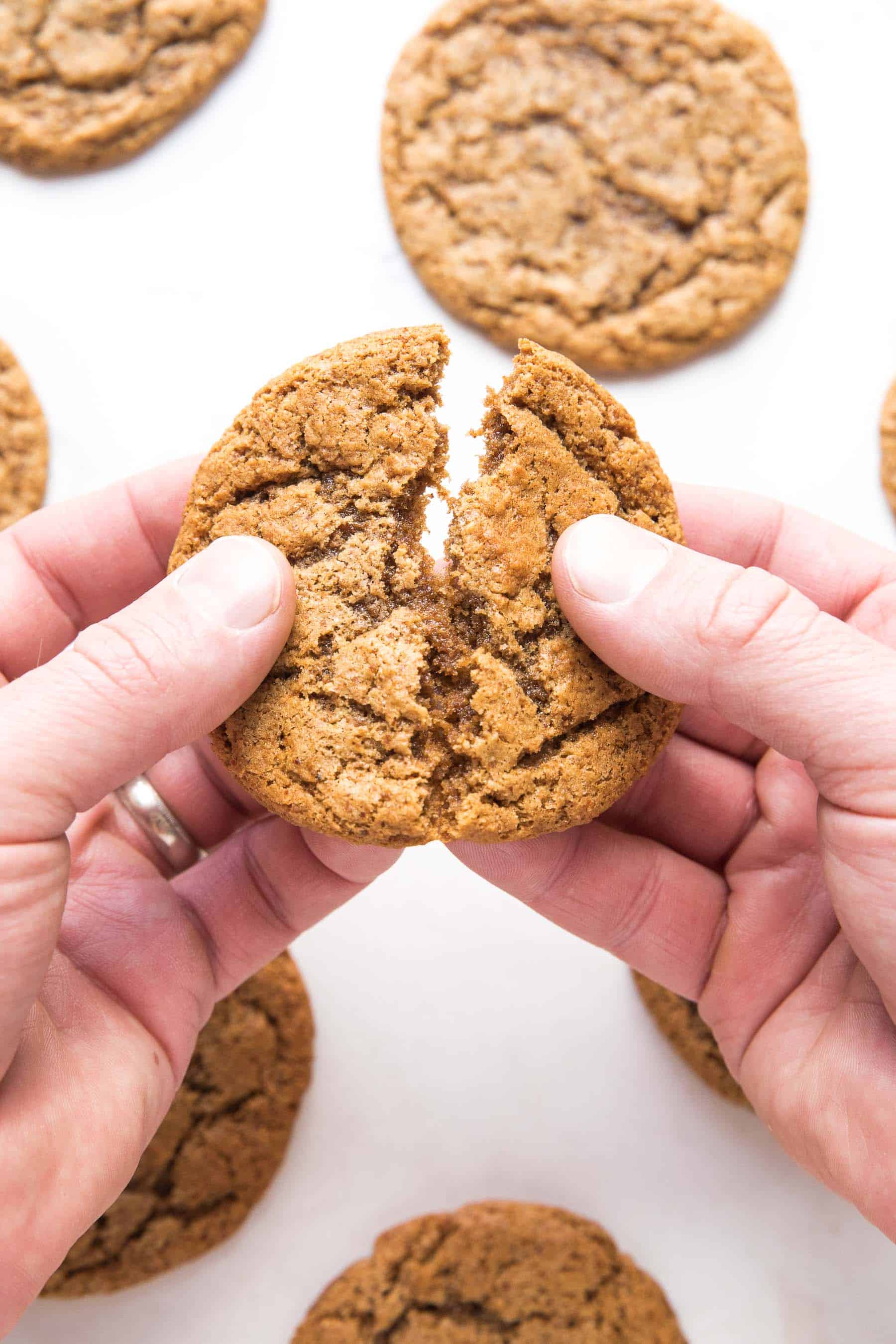 2 hands breaking an almond butter cookie on a white background