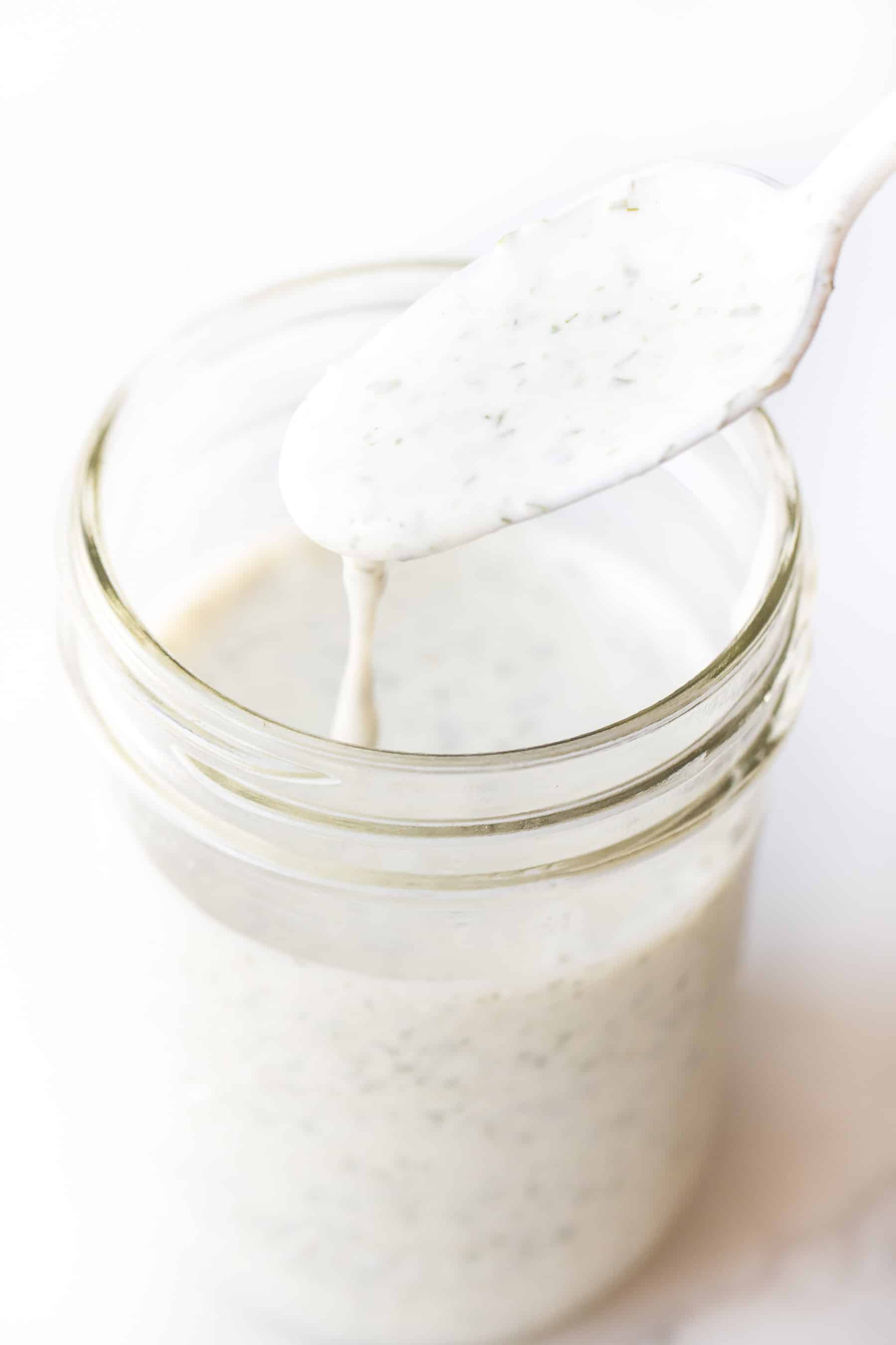 a spoon dripping ranch dressing into a mason jar on a white background