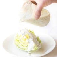 A jar of ranch being poured over iceberg lettuce on a white background