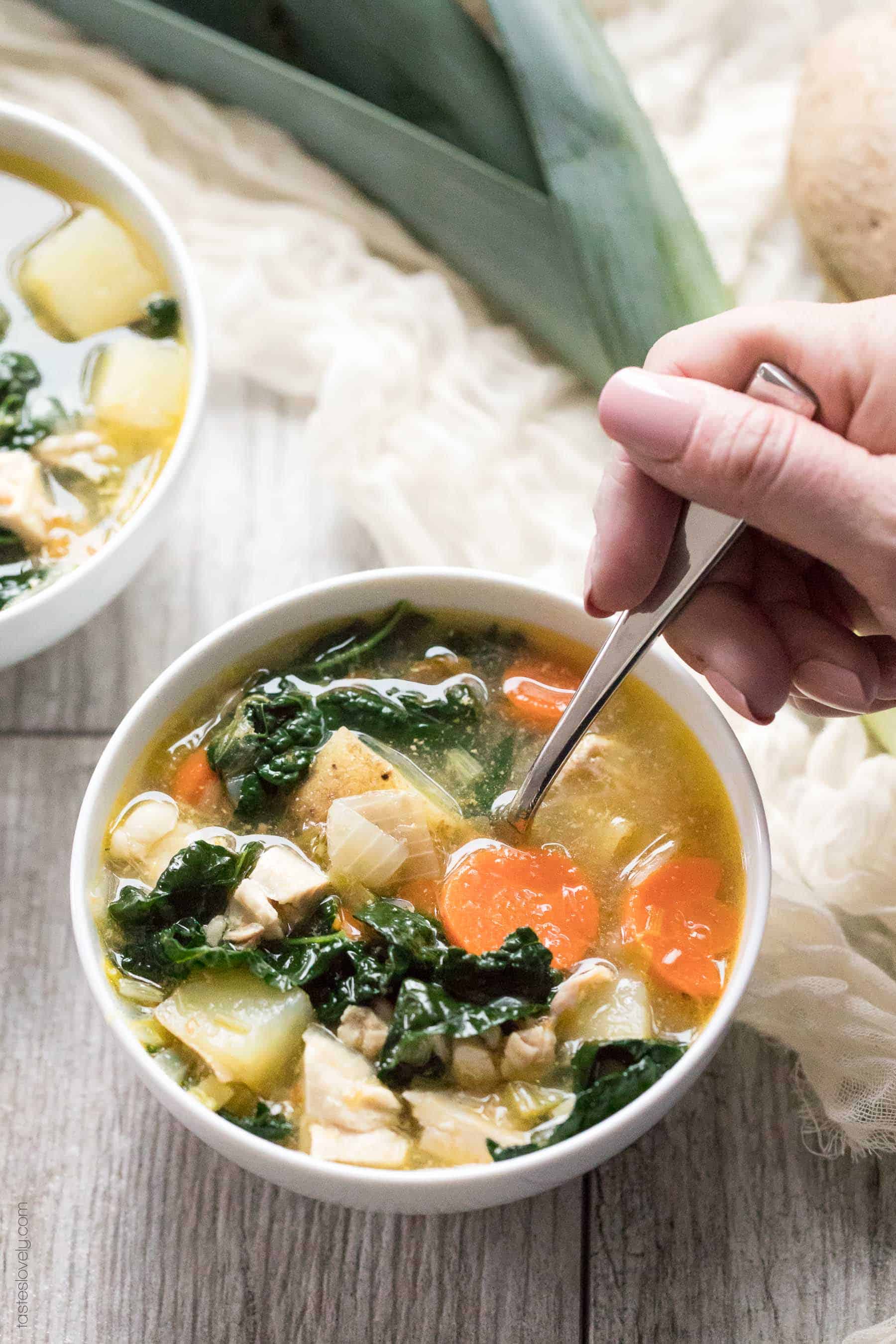 a bowl of healthy potato and leek soup in a white bowl with a hand dipping a spoon into one of the bowls