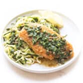 breaded lemon keto chicken piccata over zucchini noodles on a white plate and background