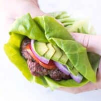 a hand holding a burger that has a lettuce wrap