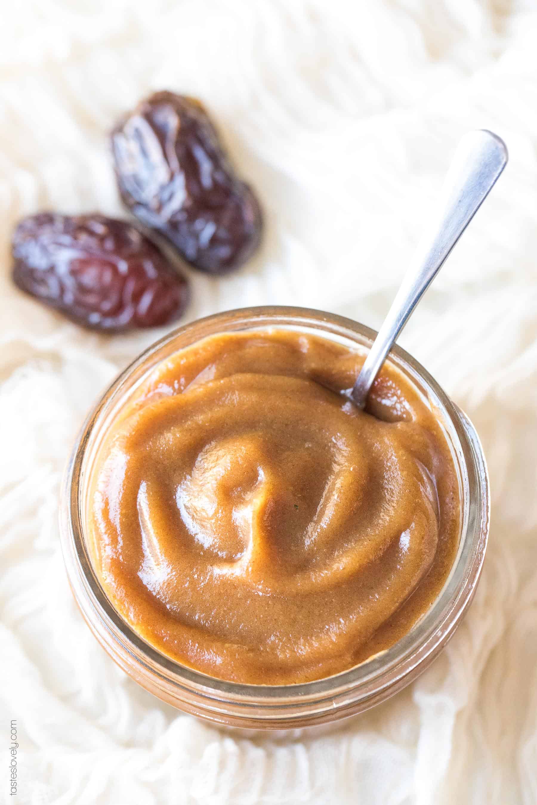 A spoon in a jar of date paste next to two medjool dates