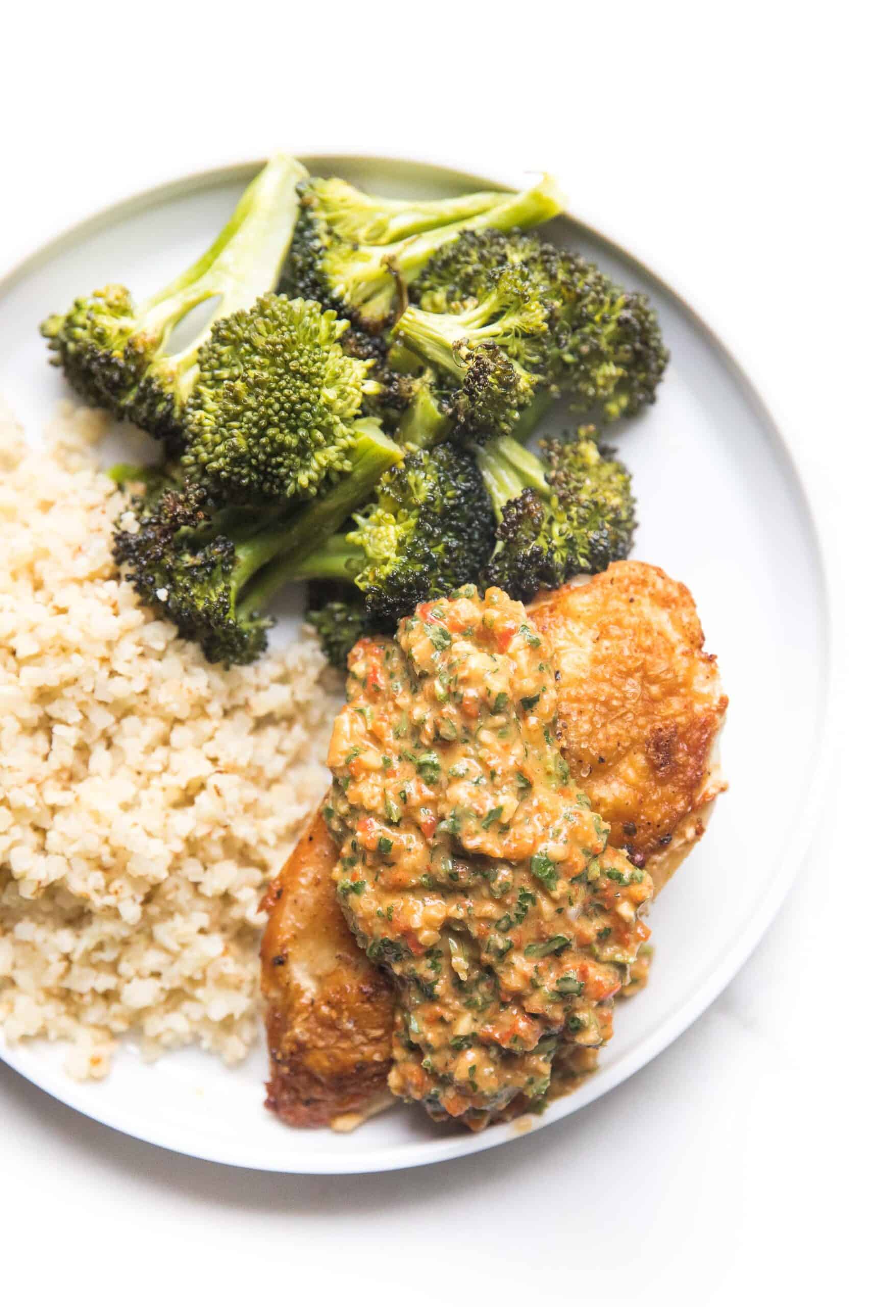 chicken topped with mediterranean salsa on a white plate with broccoli and cauliflower rice