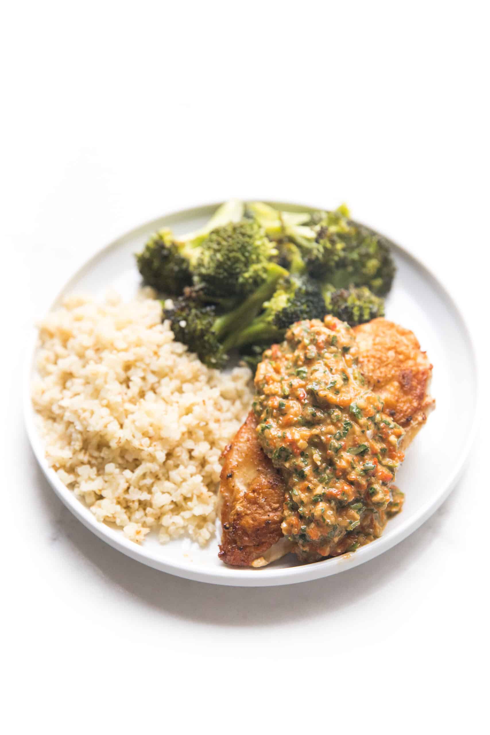 chicken topped with mediterranean salsa on a white plate with broccoli and cauliflower rice