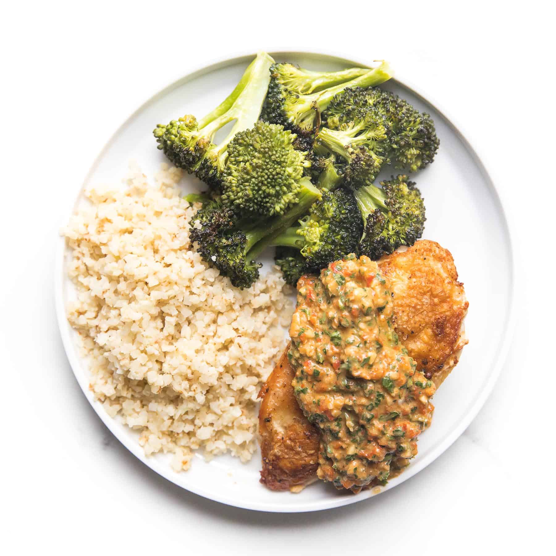 chicken topped with mediterranean salsa on a white plate with broccoli and cauliflower rice