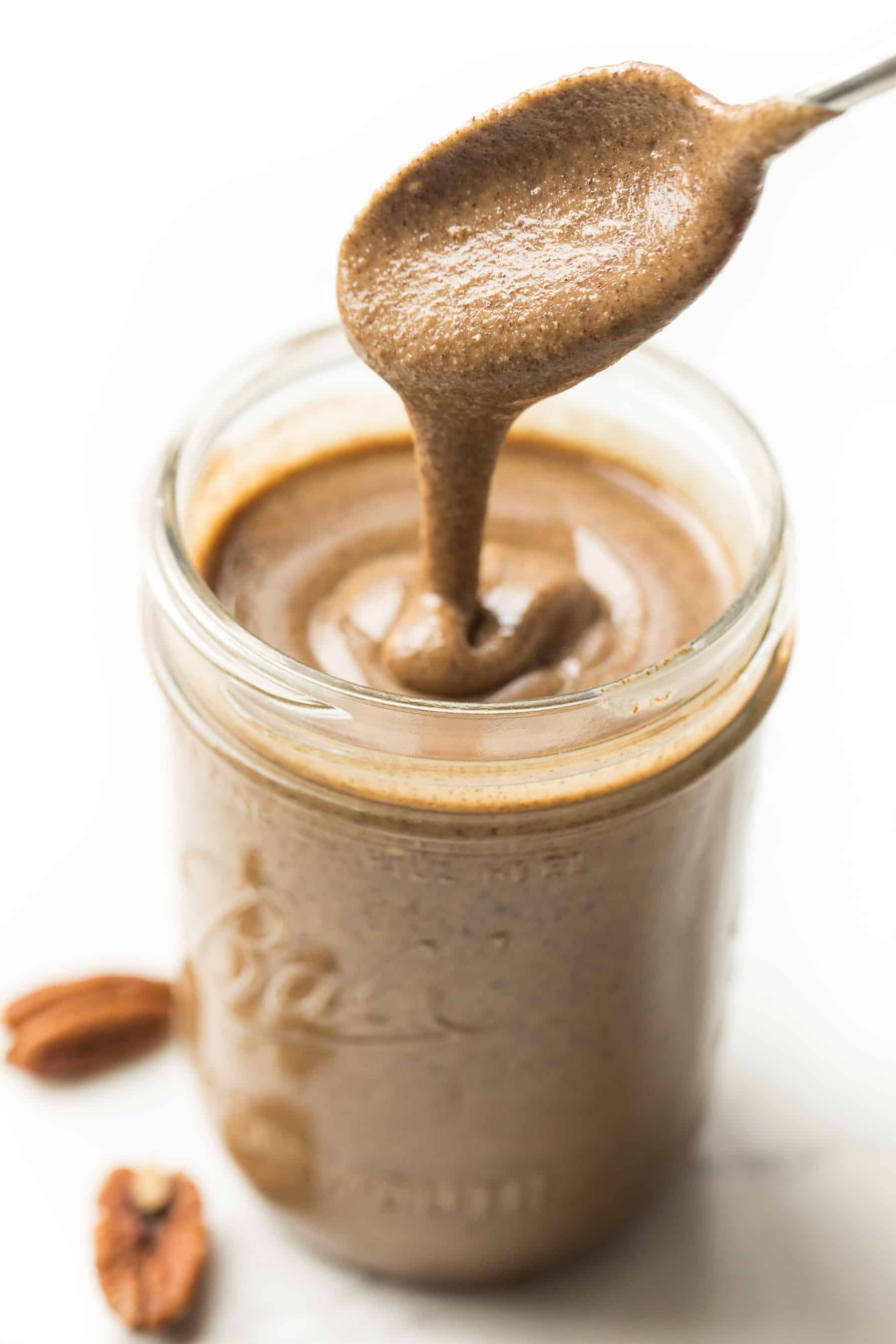 a spoon drizzling pecan butter into a mason jar