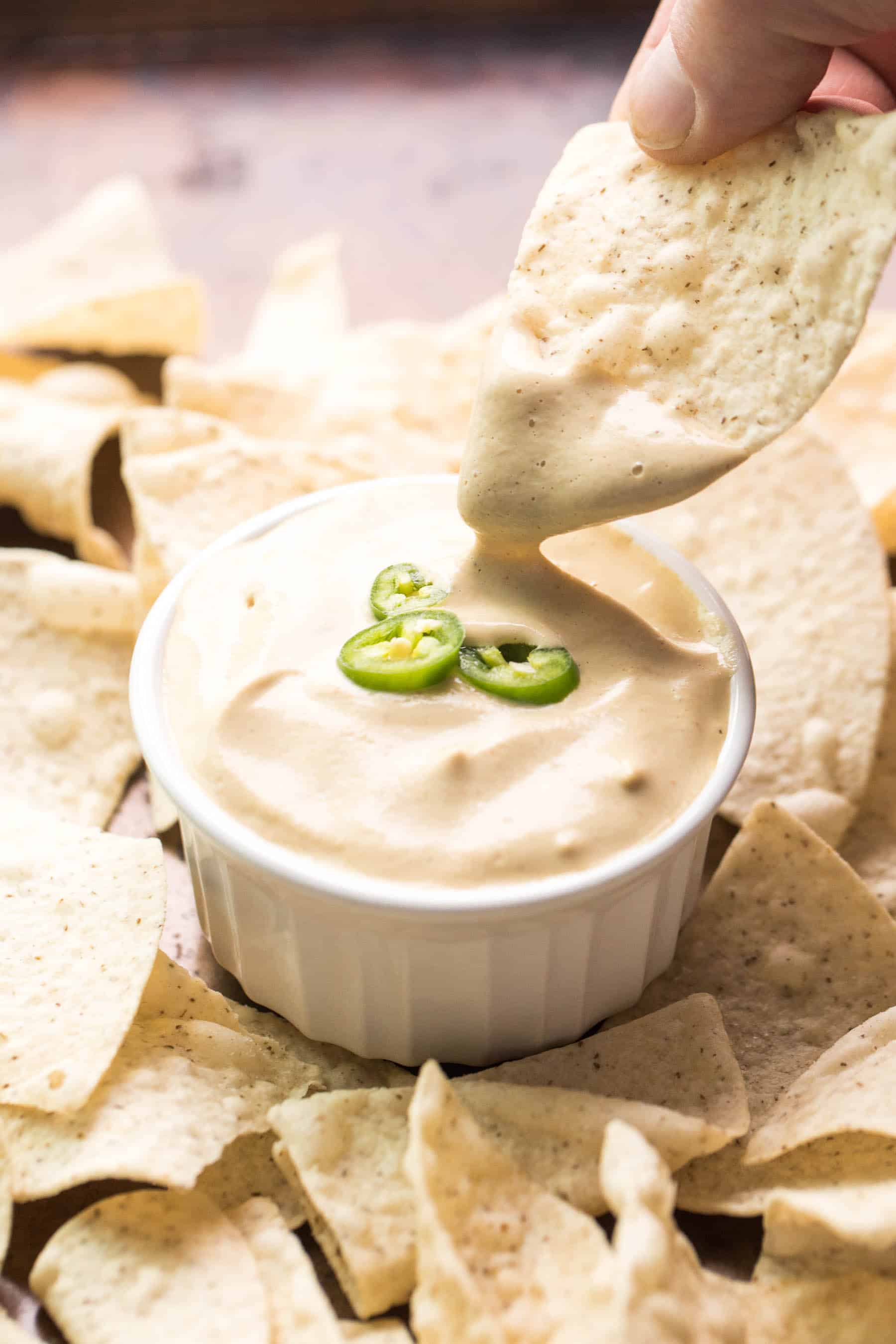 tortilla chip dipping in to a white bowl of queso nacho cheese