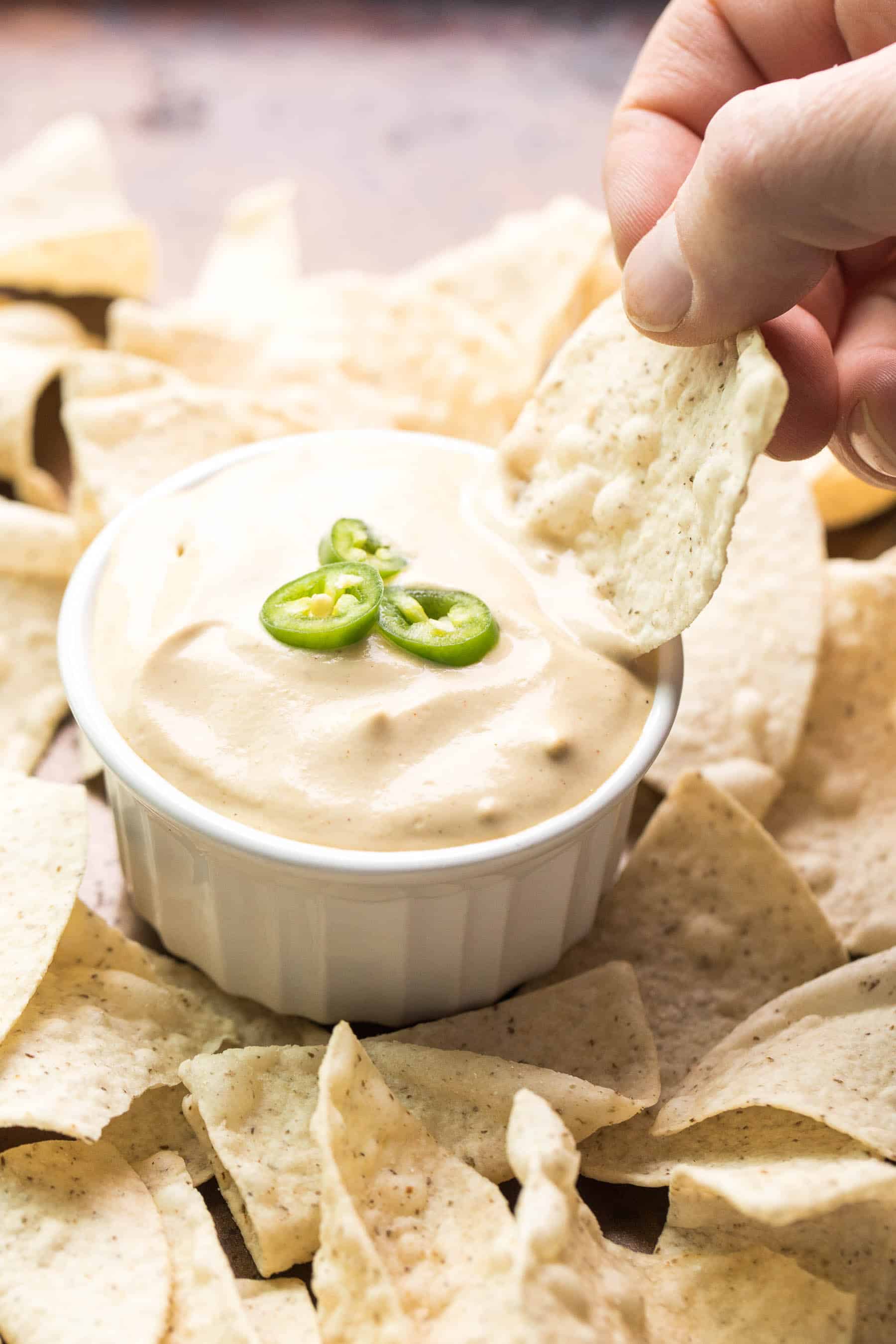 hand dipping a tortilla chip in queso nacho cheese in a white bowl