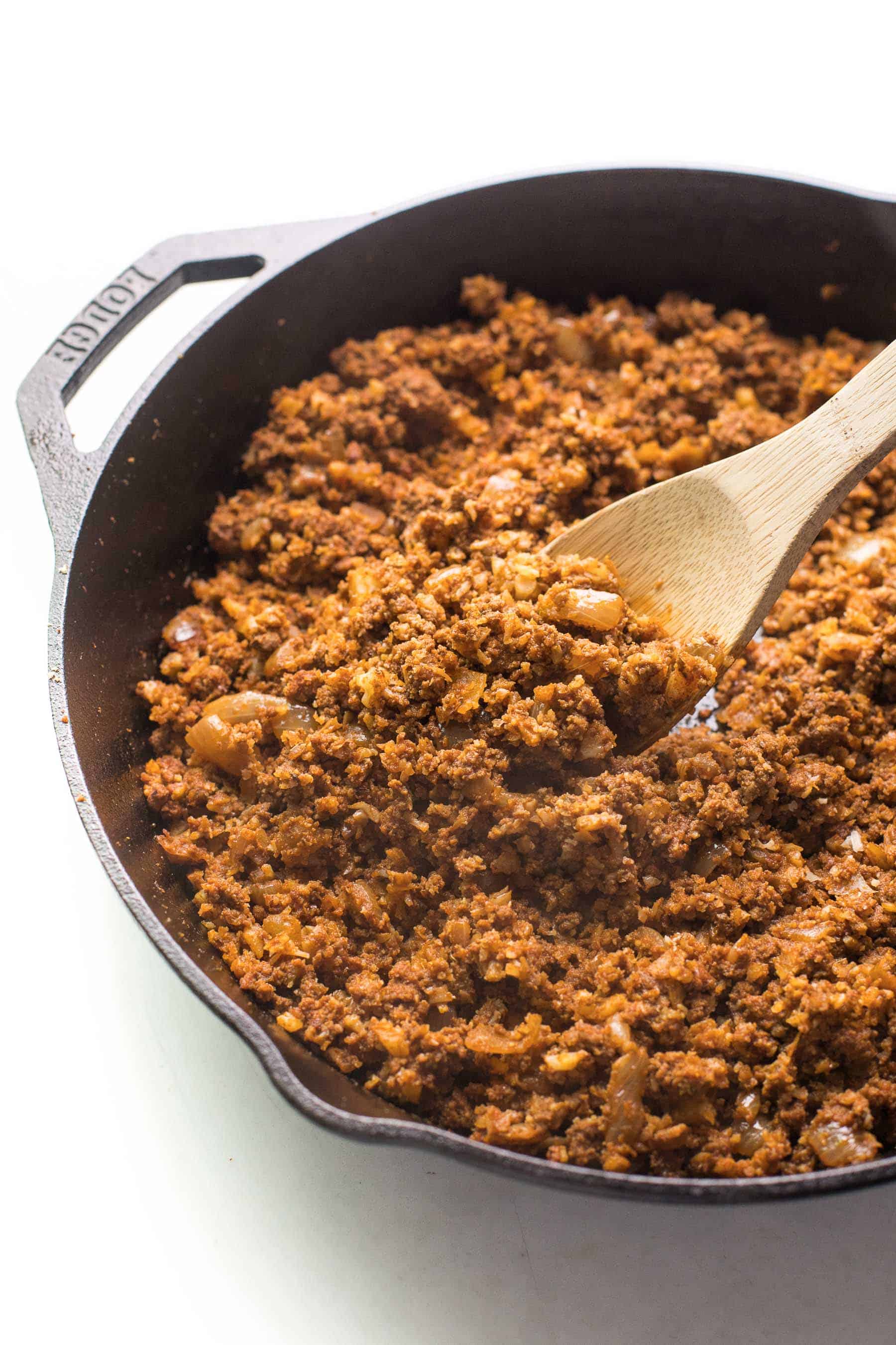 ground beef taco meat in a cast iron skillet with a spoon on a white background