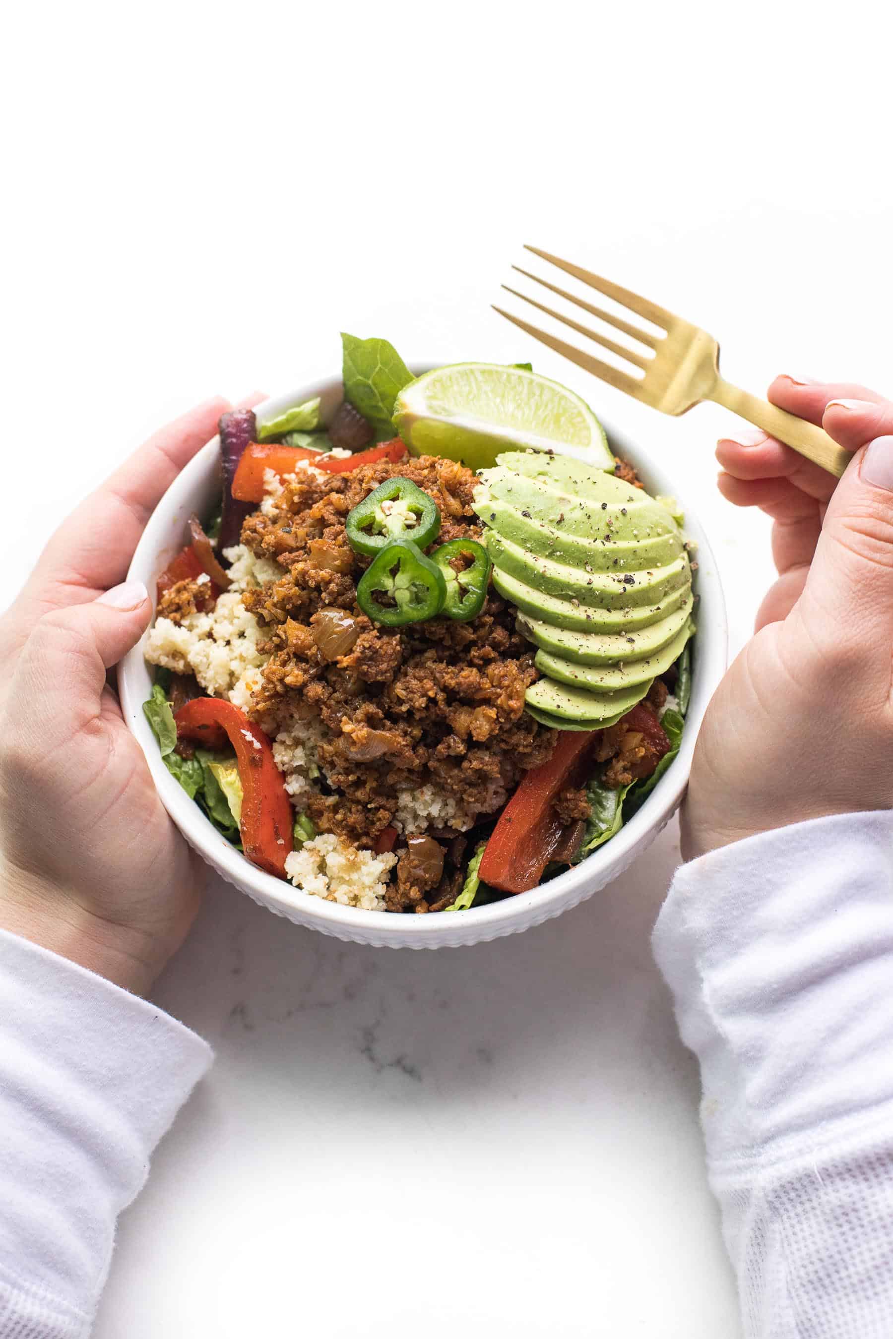 2 hands holding a burrito bowl with a gold fork in the right hand