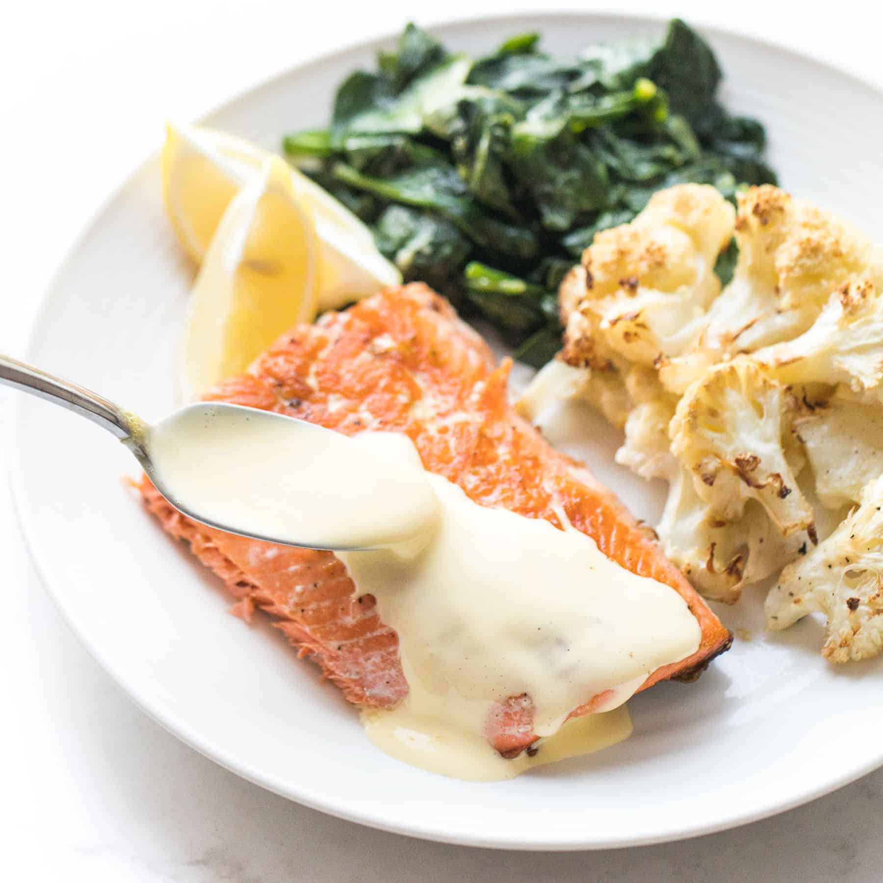 salmon with hollandaise sauce with roasted cauliflower and cooked spinach on a white plate