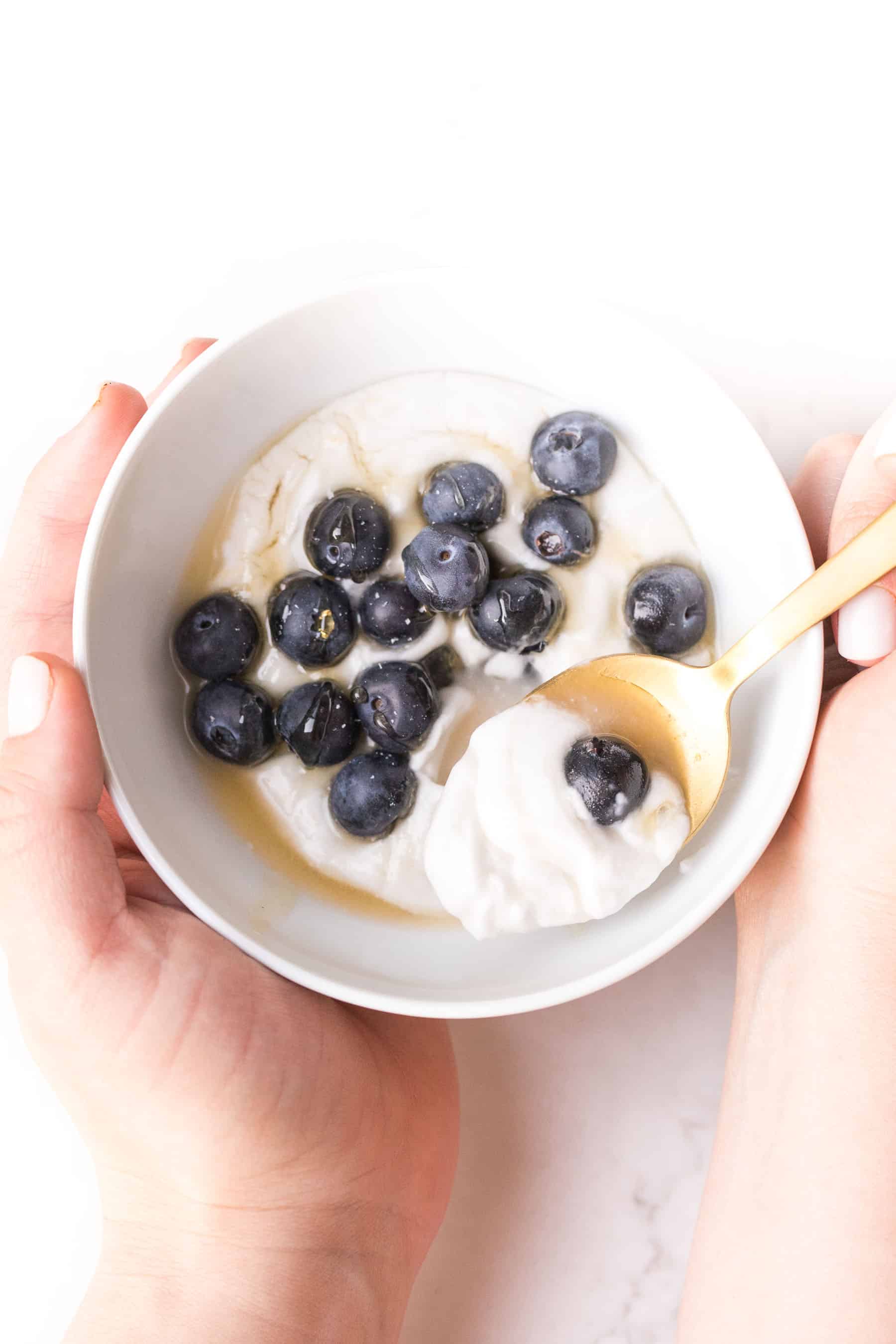 white bowl on a white background with coconut whipped cream, blueberries and honey