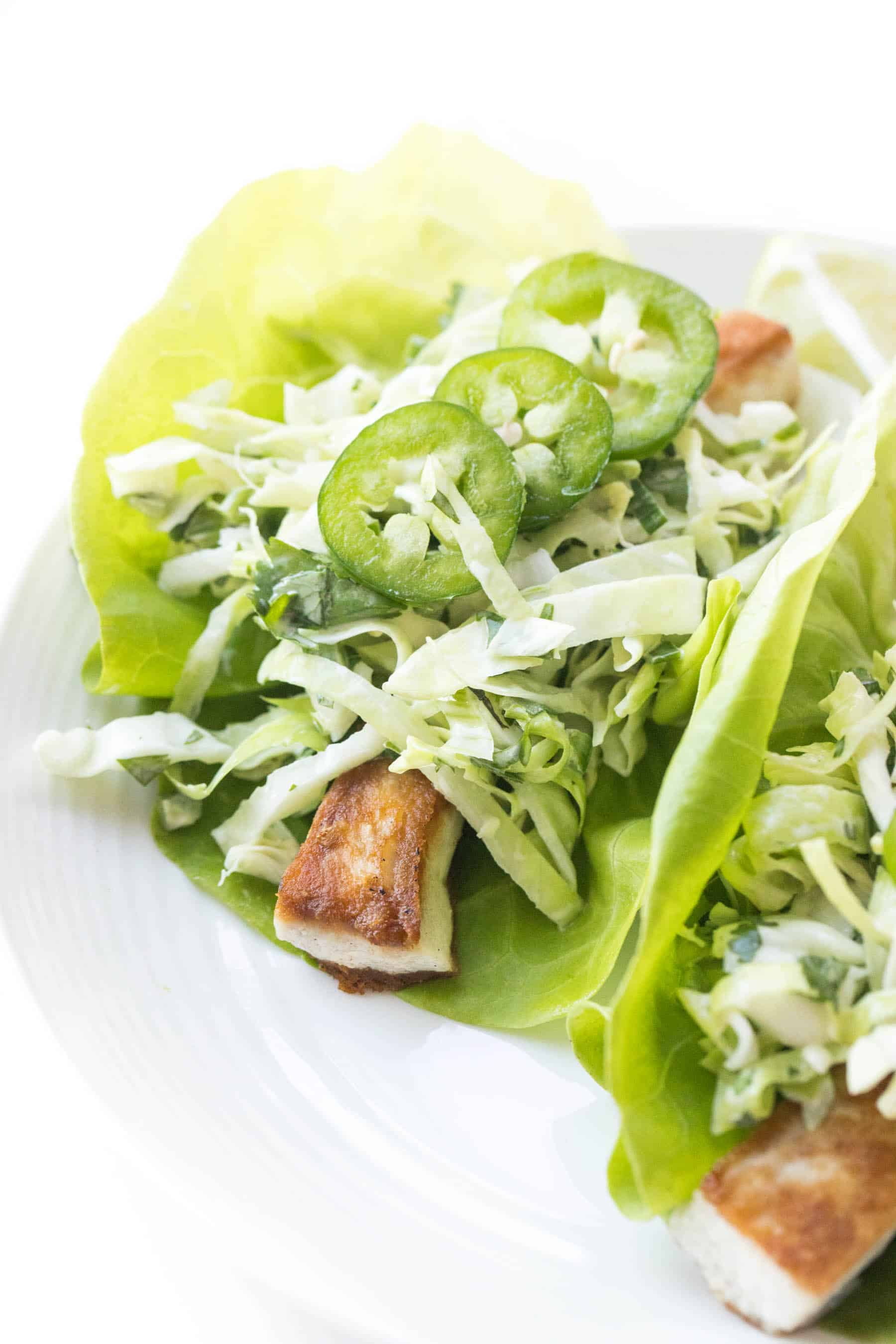 fish tacos on a lettuce taco shell topped with coleslaw on a white background