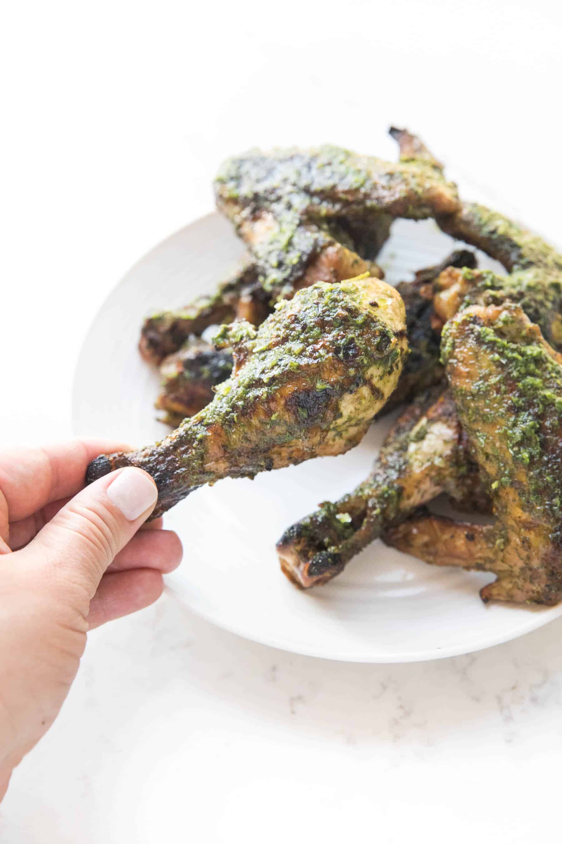 hand holding chicken drumstick with chimichurri sauce on white background