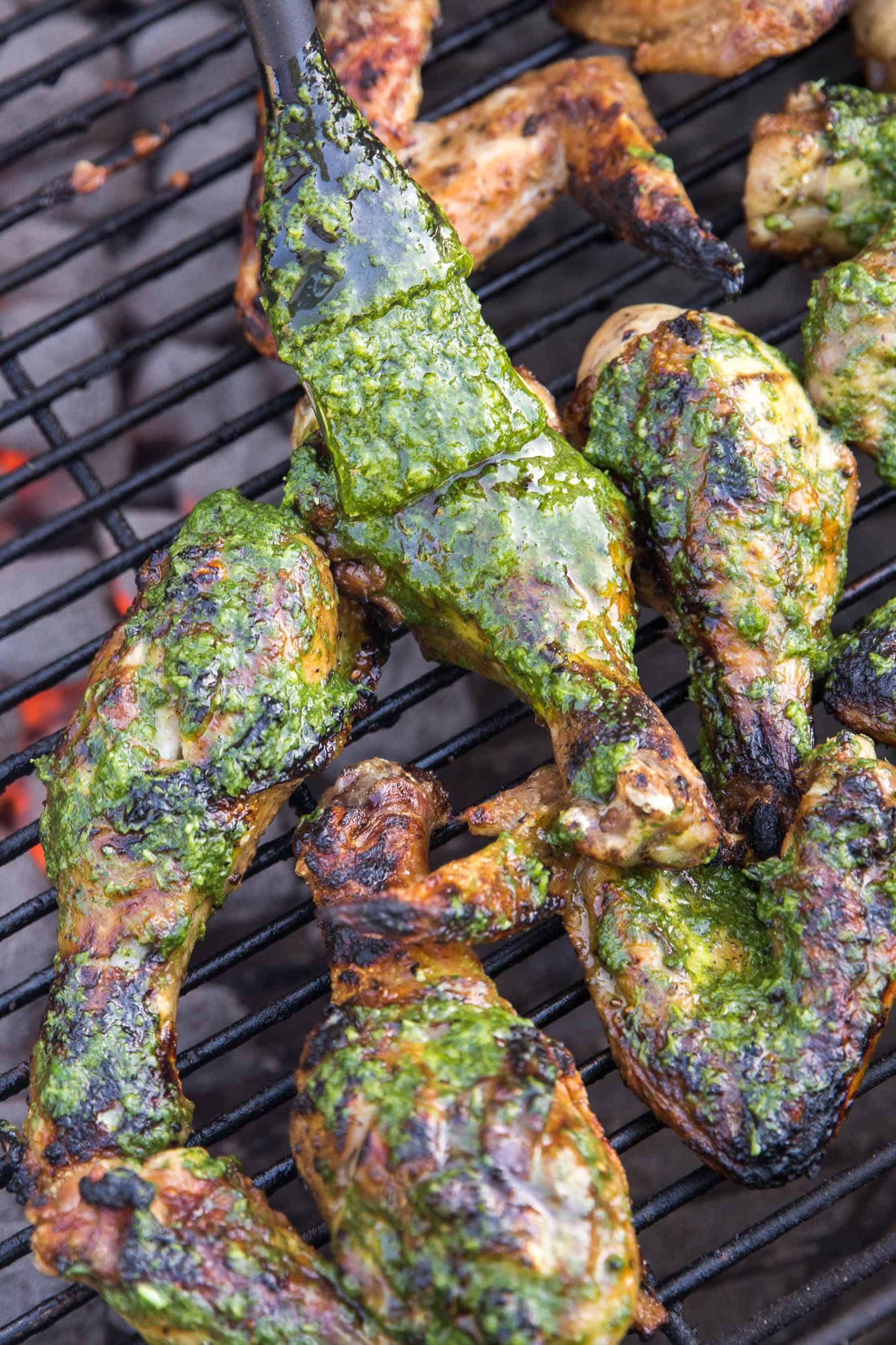 grilled chicken being brushed with green chimichurri sauce on a bbq