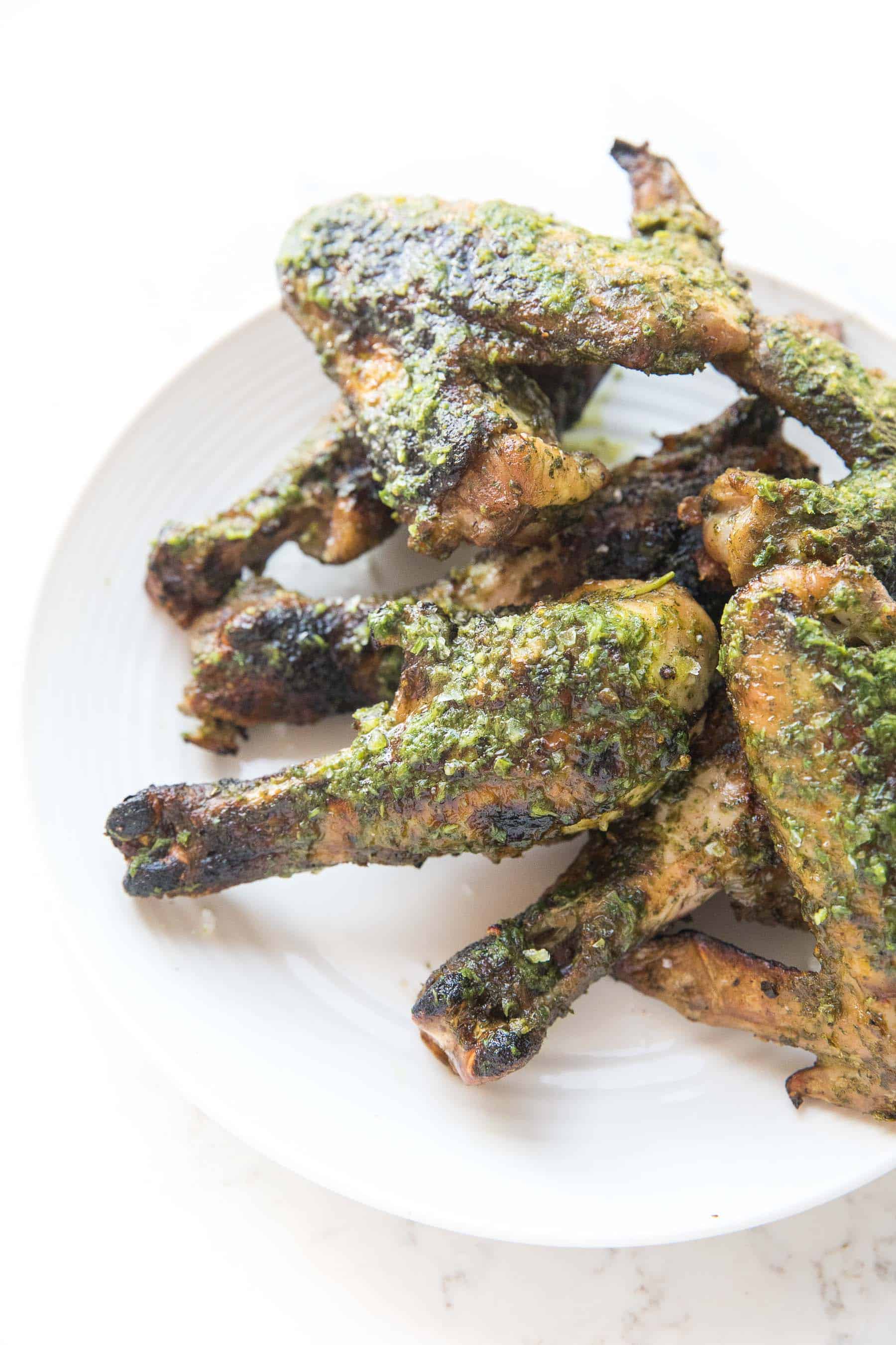 grilled chicken drumsticks and wings brushed with chimichurri sauce on a white background and white plate