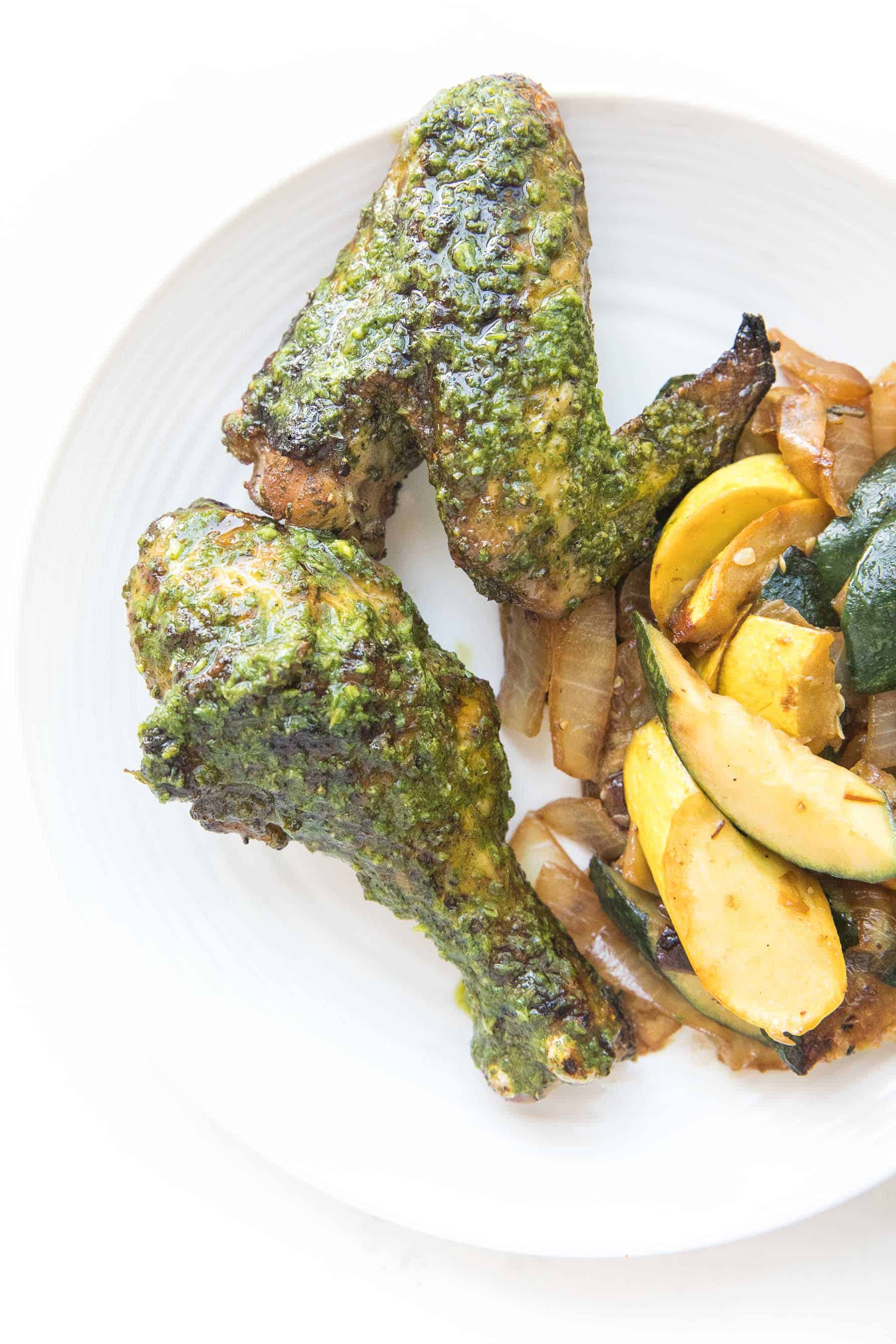 white plate of grilled chicken drumsticks and wings and squash on a white background