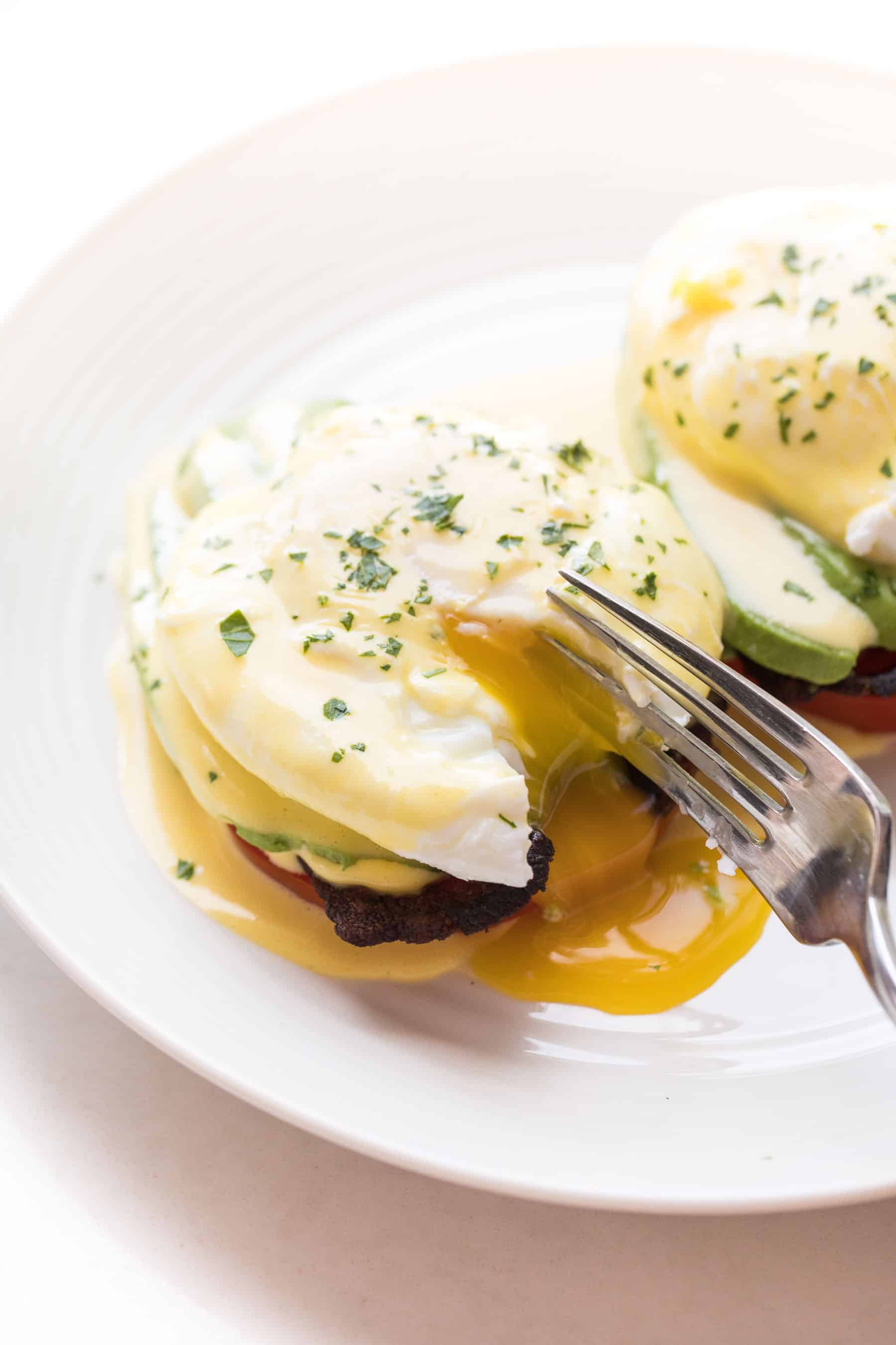 Fork cutting in to eggs benedict on a white plate