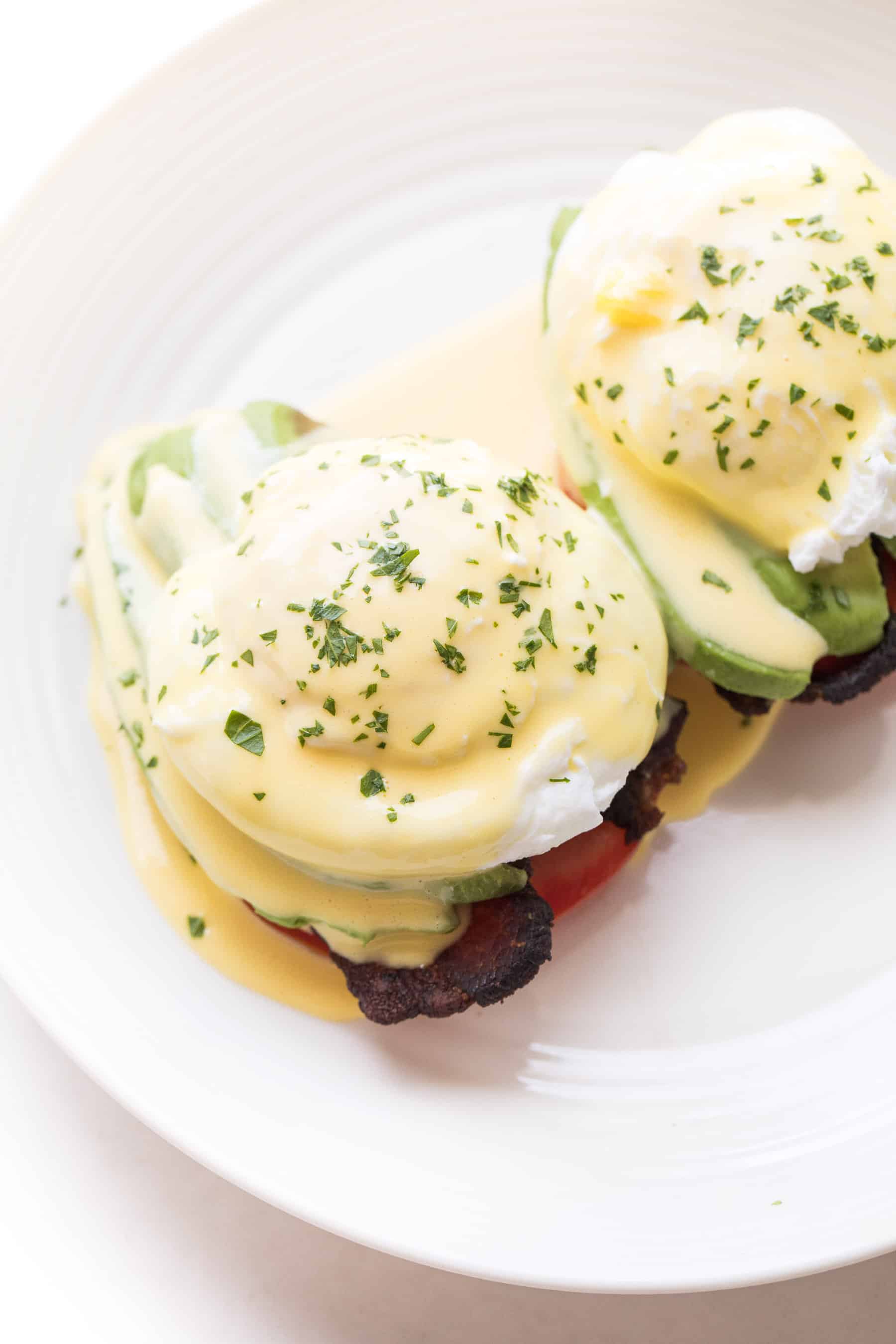 Fork cutting in to eggs benedict on a white plate