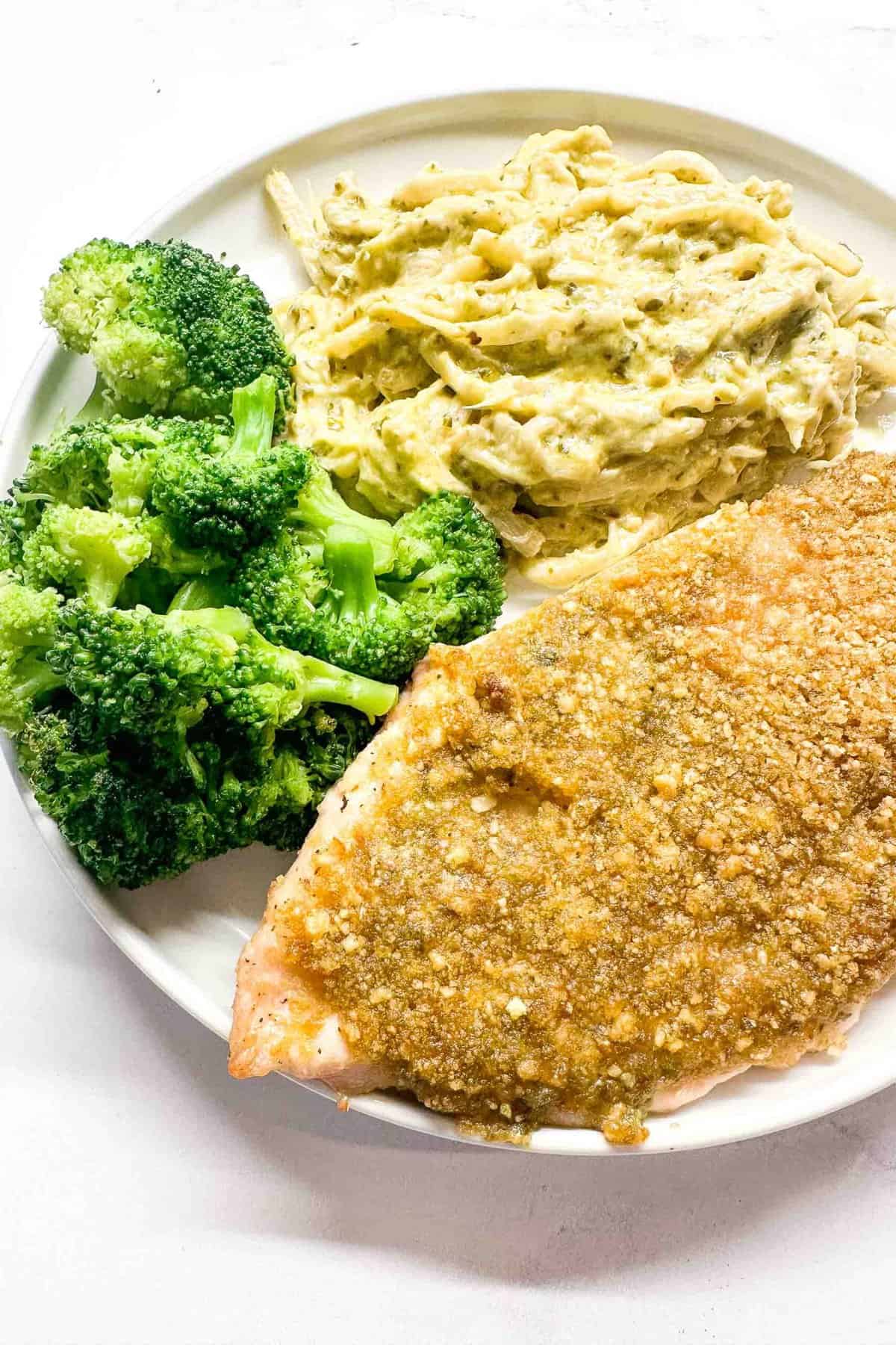 crispy baked pesto chicken recipe on a plate next to broccoli and mashed cauliflower