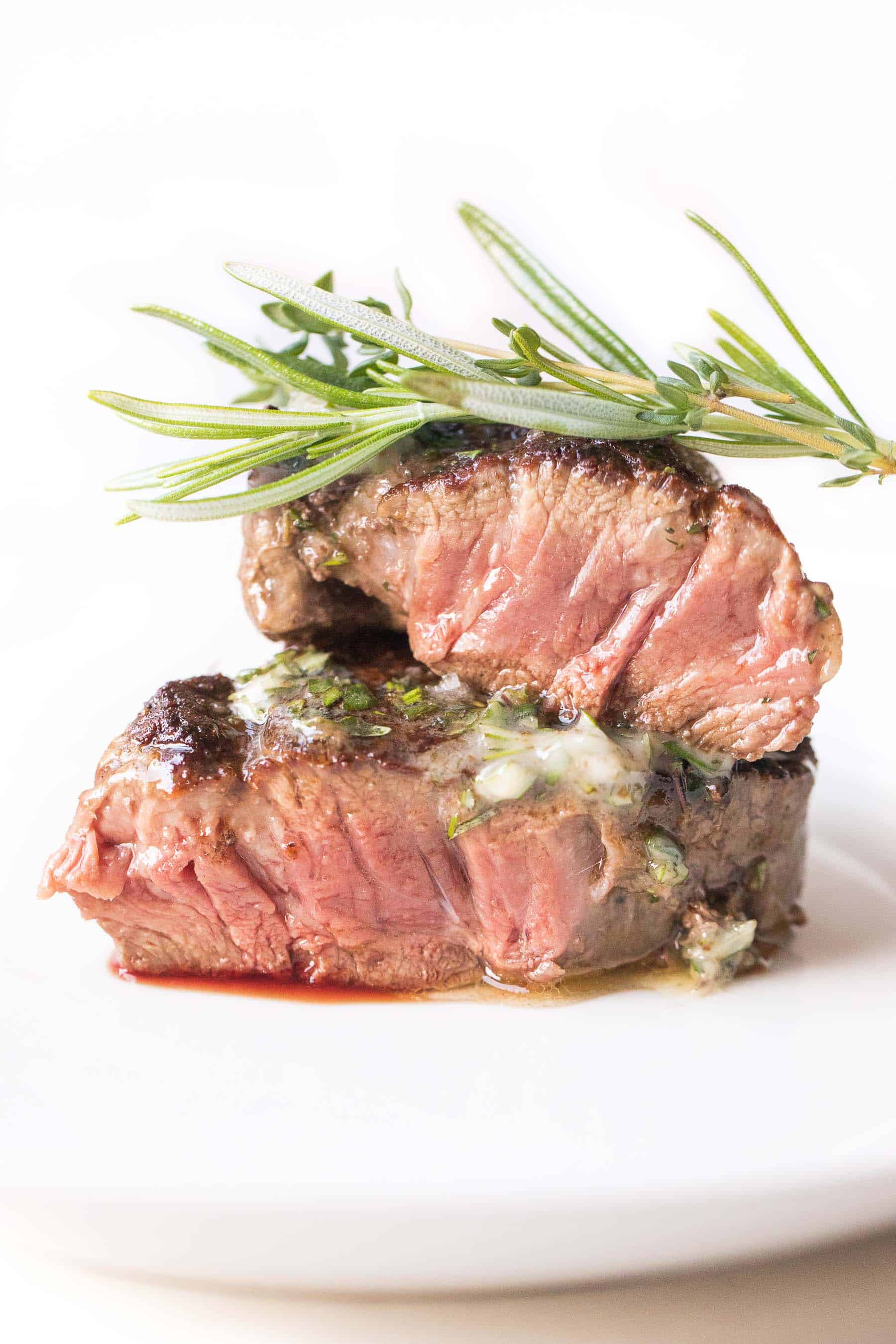 Filet mignon topped with herb butter on a white plate and white background