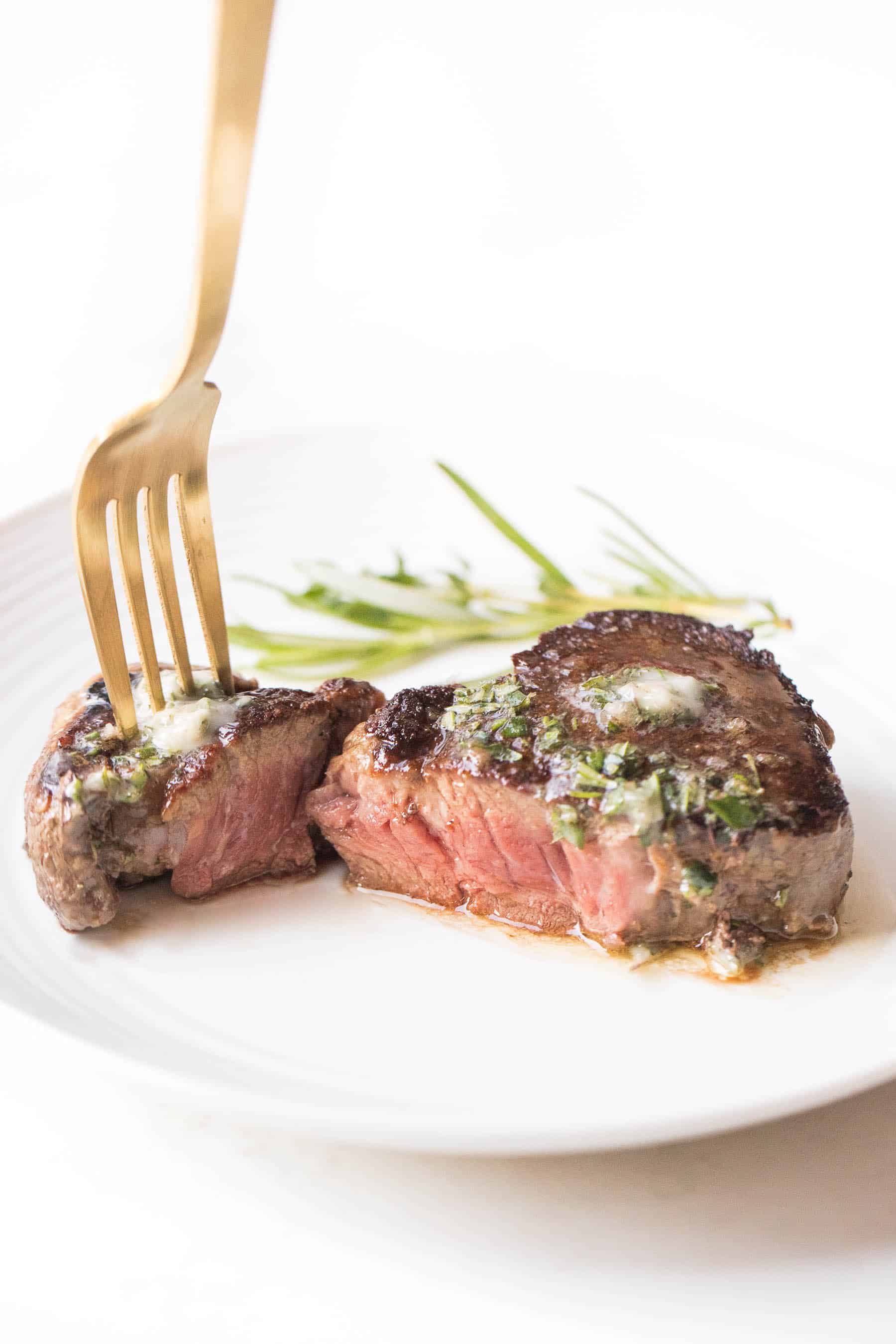 Filet mignon cut in half topped with herb butter on a white plate and white background