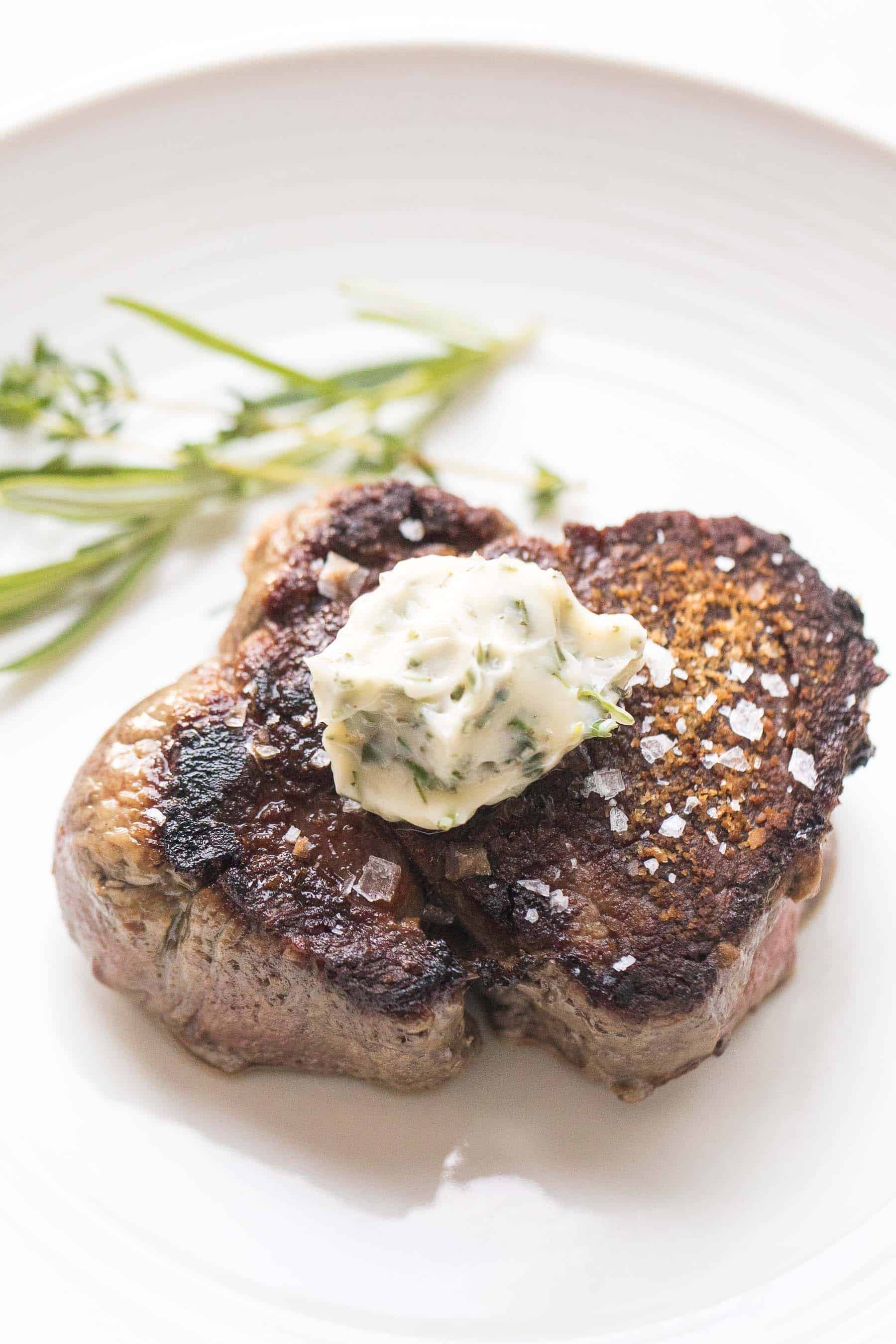 Filet mignon topped with herb butter on a white plate and white background