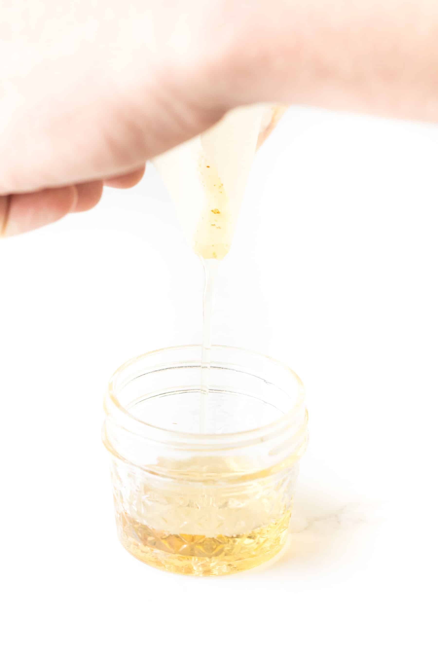pouring bacon grease into a mason jar on a white background