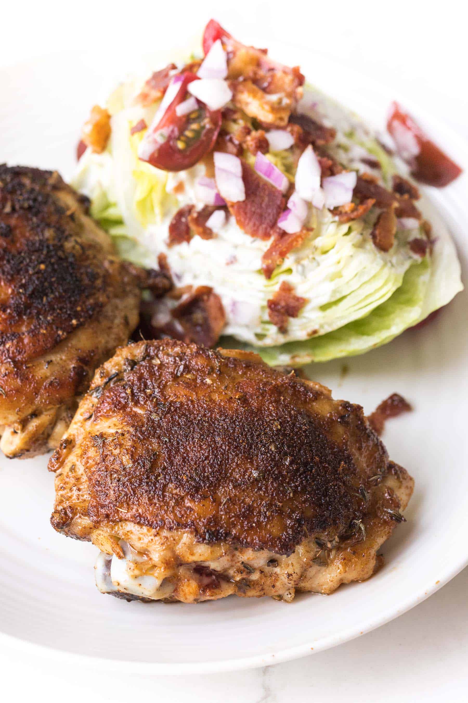 cajun chicken thighs with a wedge salad on a white plate and white background