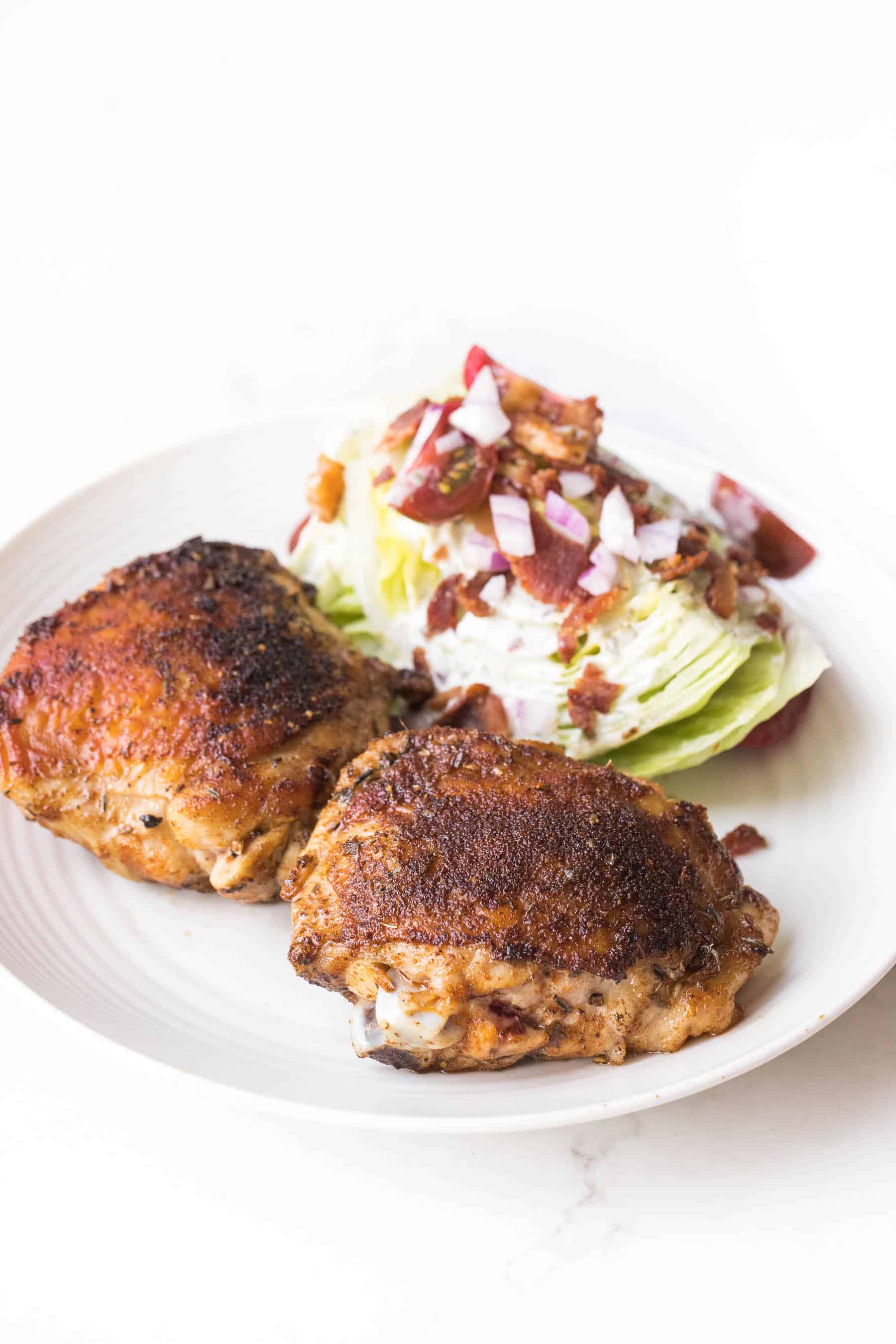 cajun chicken thighs with a wedge salad on a white plate and white background