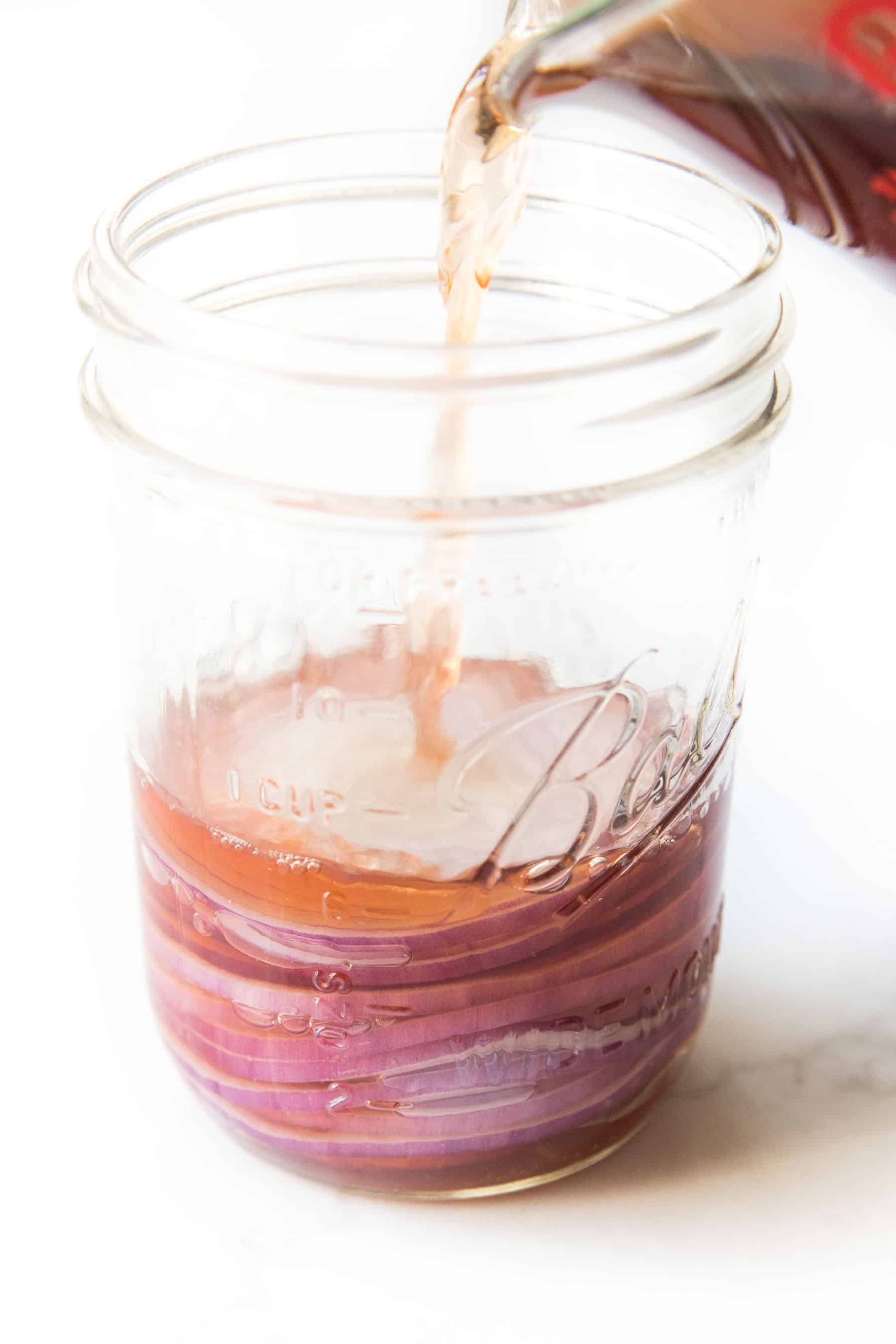 pouring red wine vinegar over pickled onions on a white background