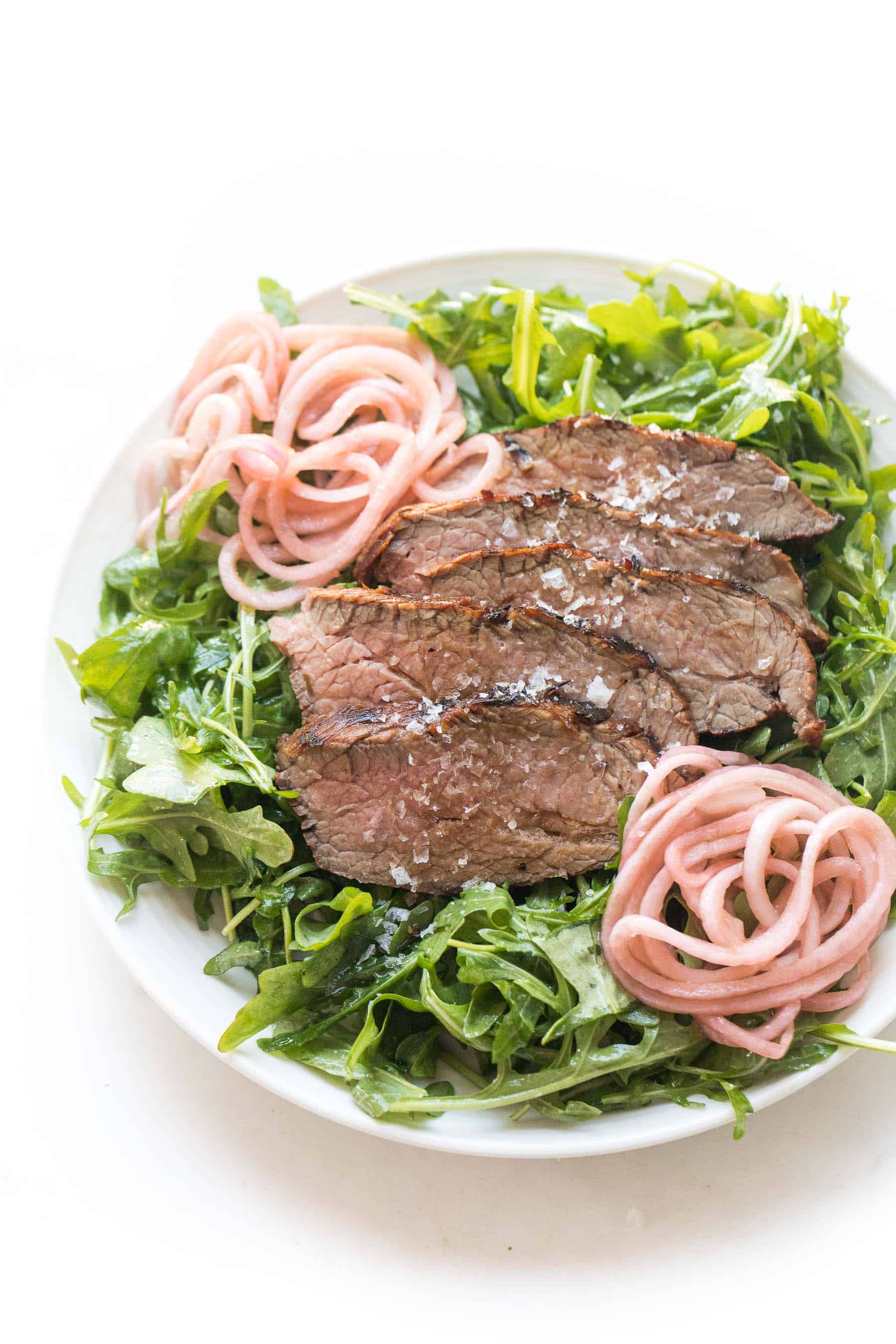 Tri tip arugula salad with pickled onions on a white plate and white background