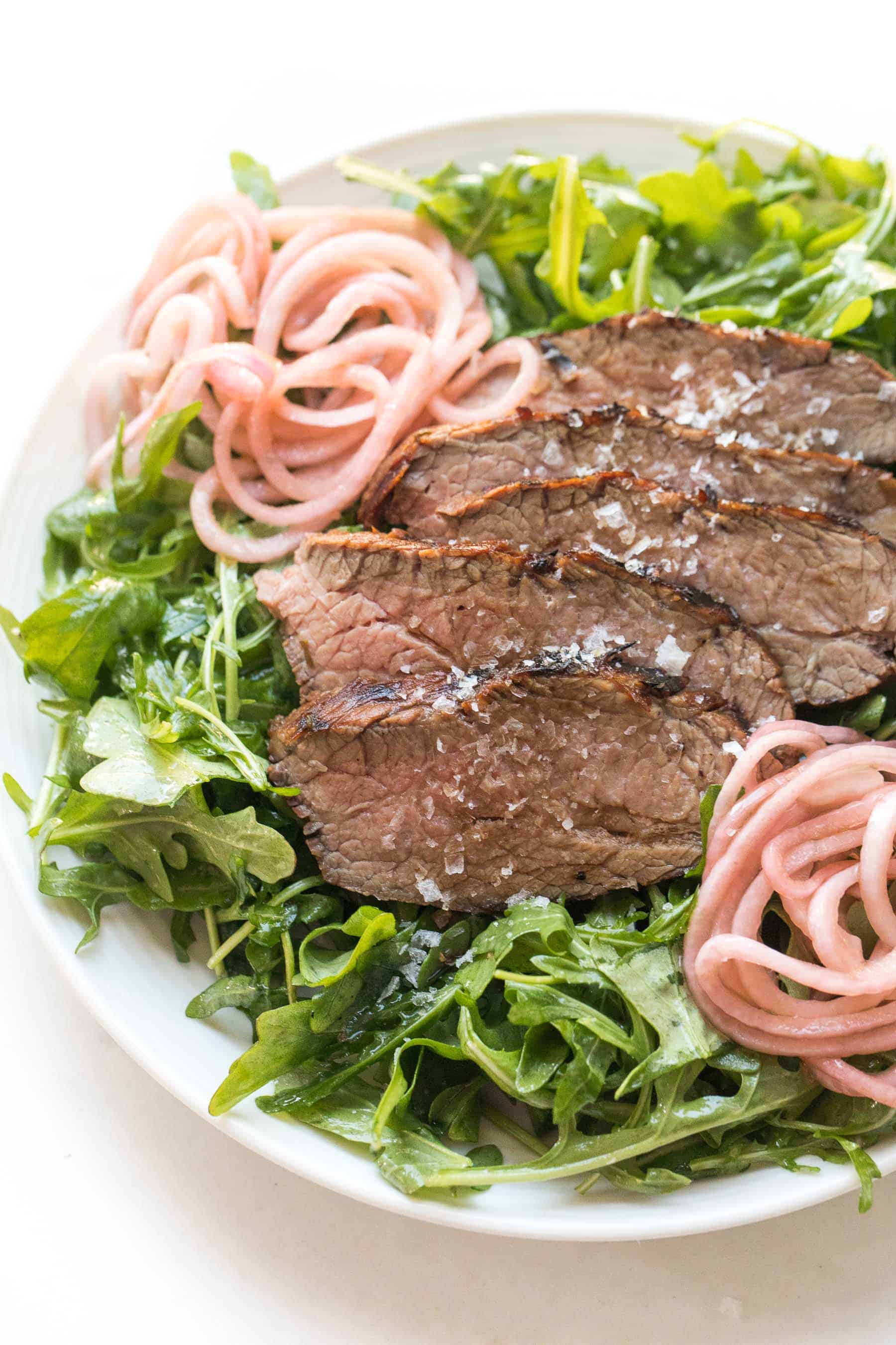 Tri tip arugula salad with pickled onions on a white plate and white background