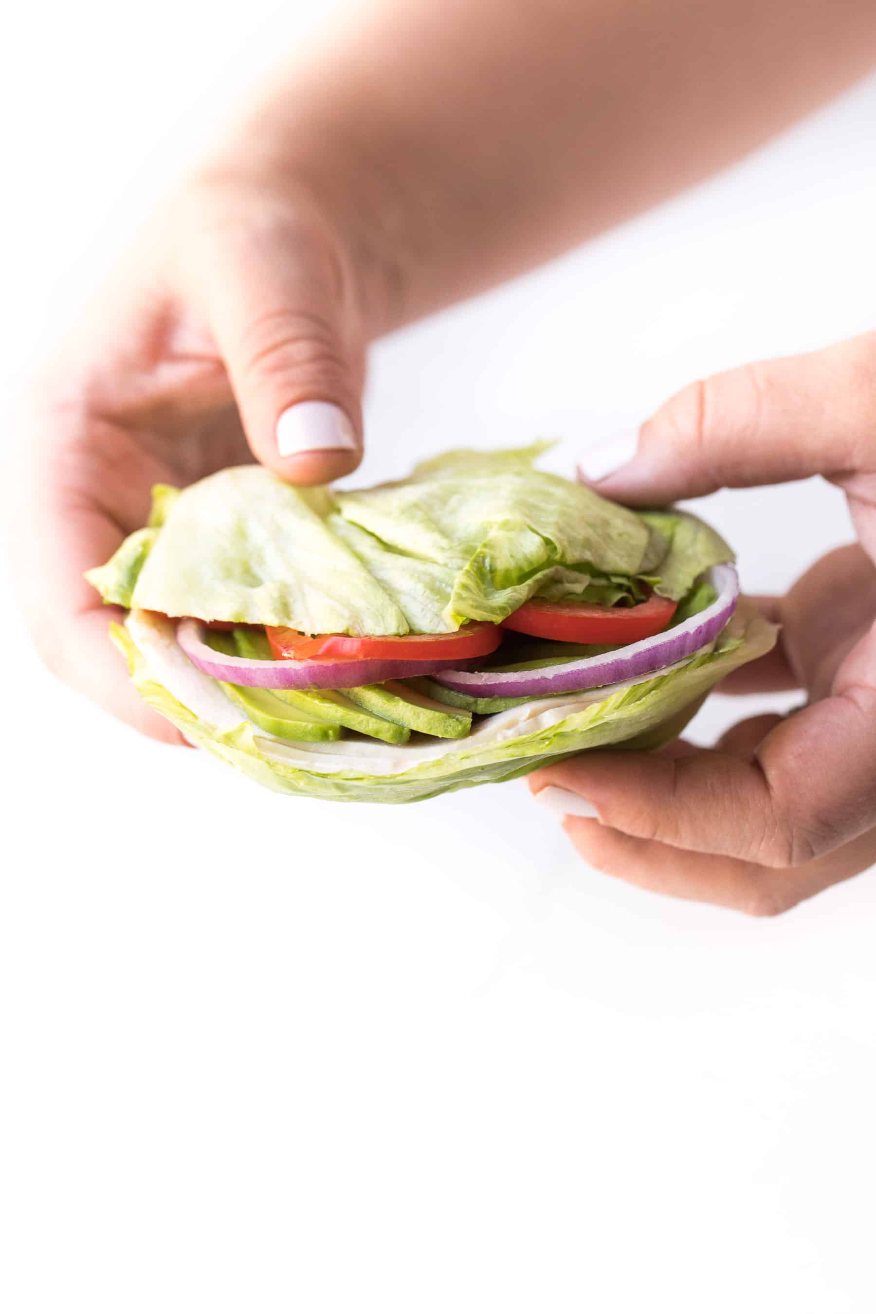 hand holding an iceberg lettuce wrapped sandwich