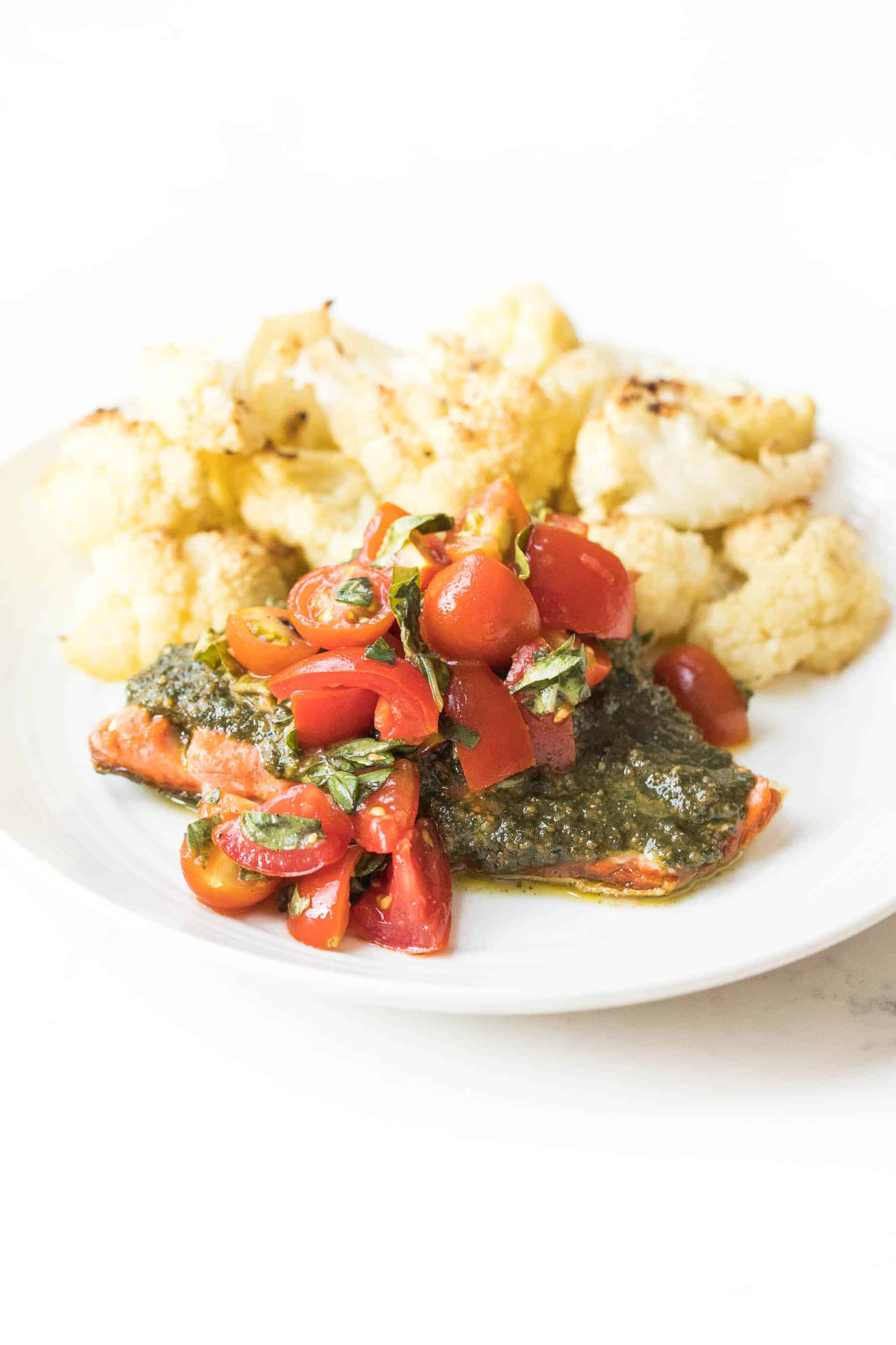 salmon topped with pesto and tomatoes on a white plate and white background