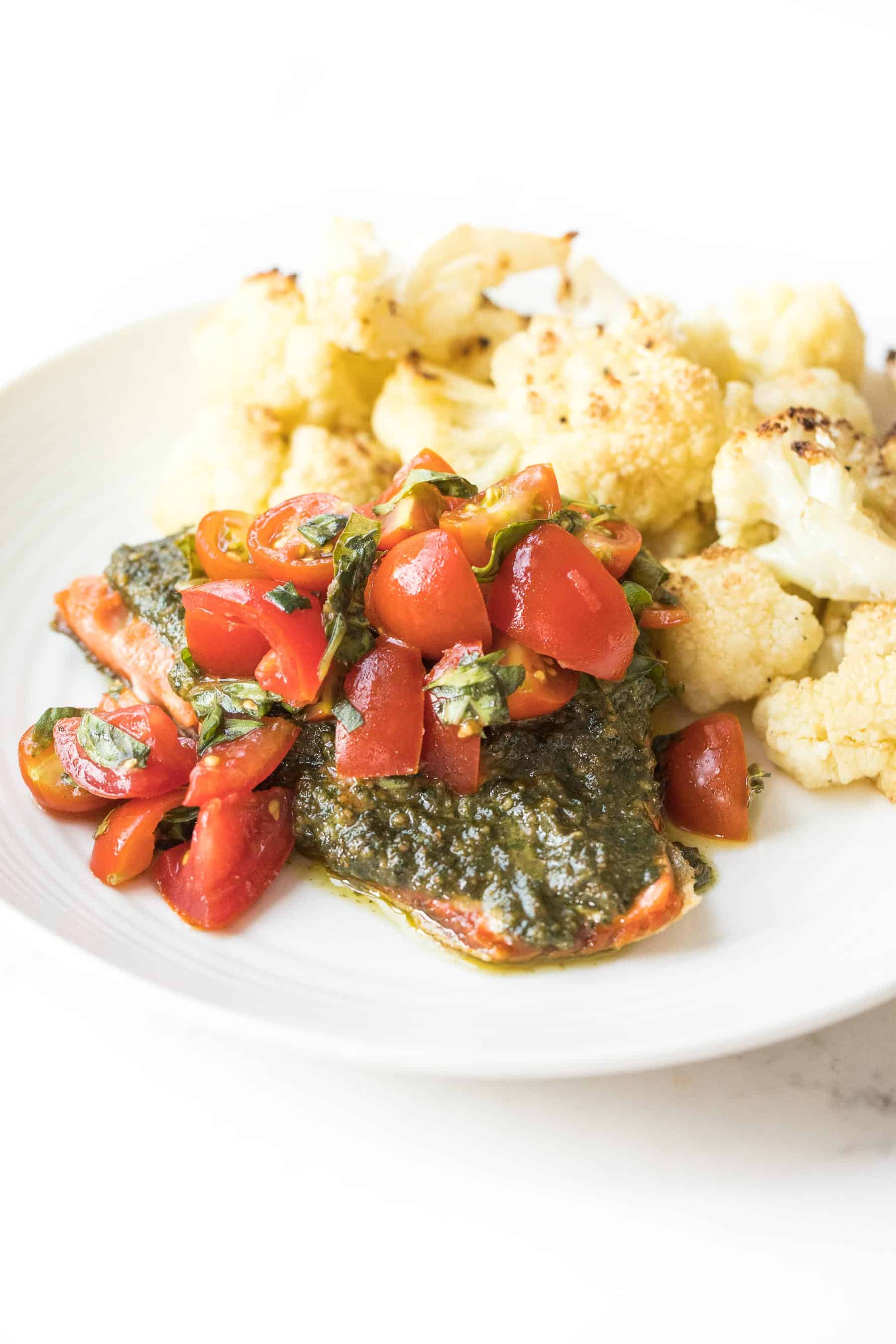 salmon topped with pesto and tomatoes on a white plate and white background