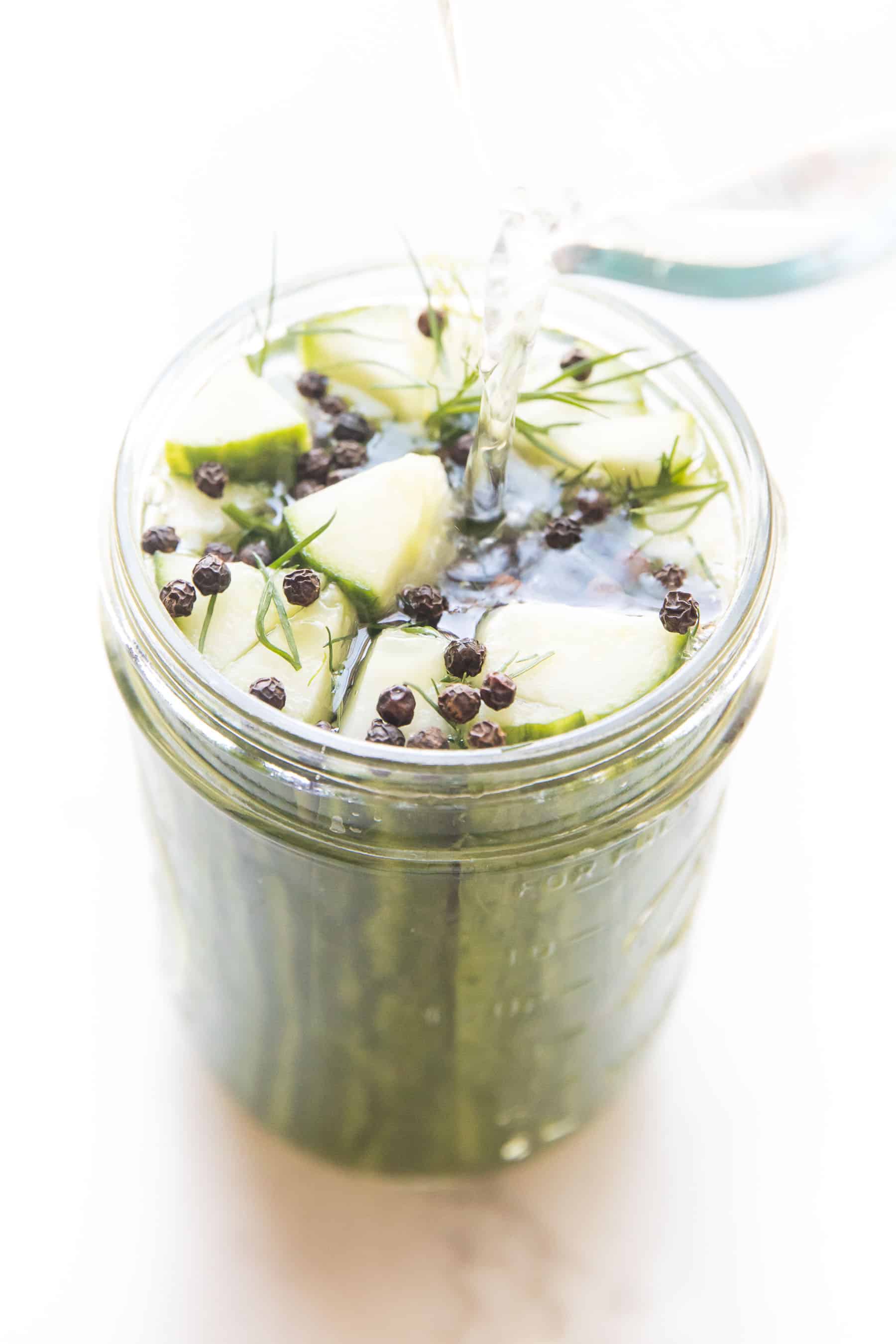 brining liquid being poured over homemade pickles in a mason jar