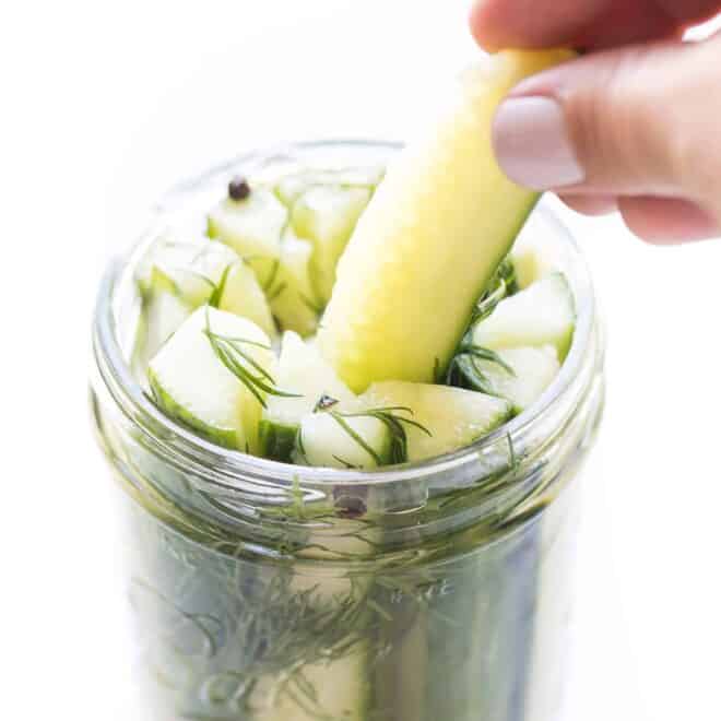 a hand pulling out a pickle spear from a mason jar