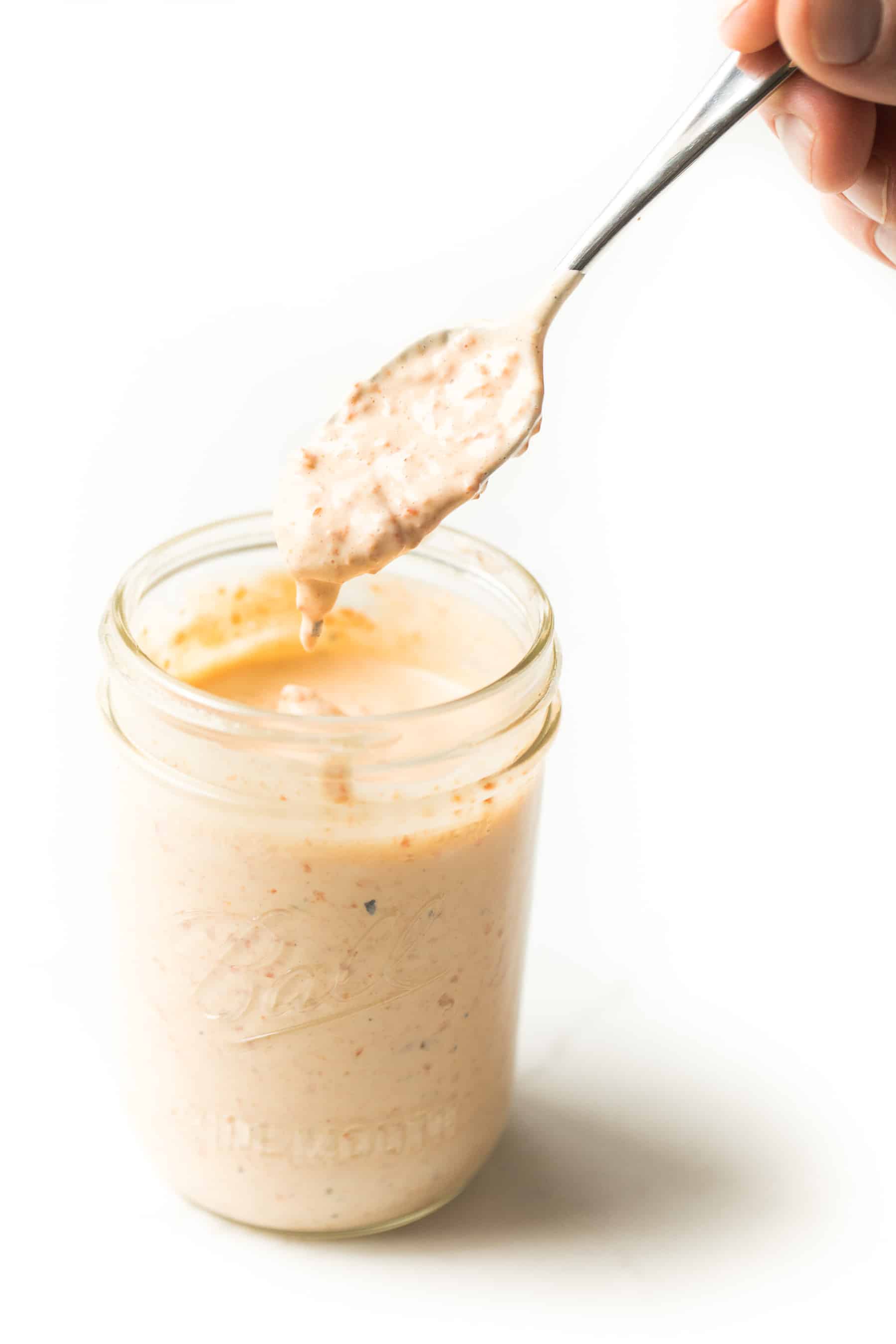 Spoon scooping out red pepper mayonnaise from a mason jar