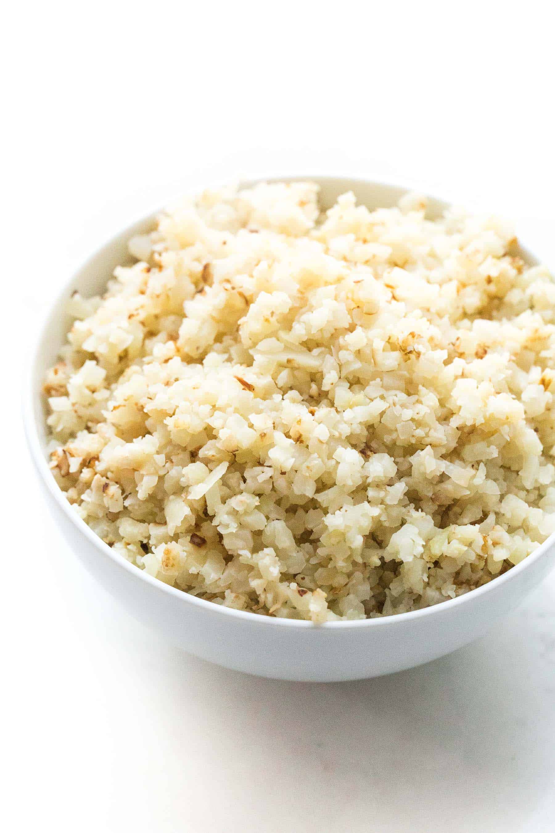 cooked cauliflower rice in a white bowl on a white background