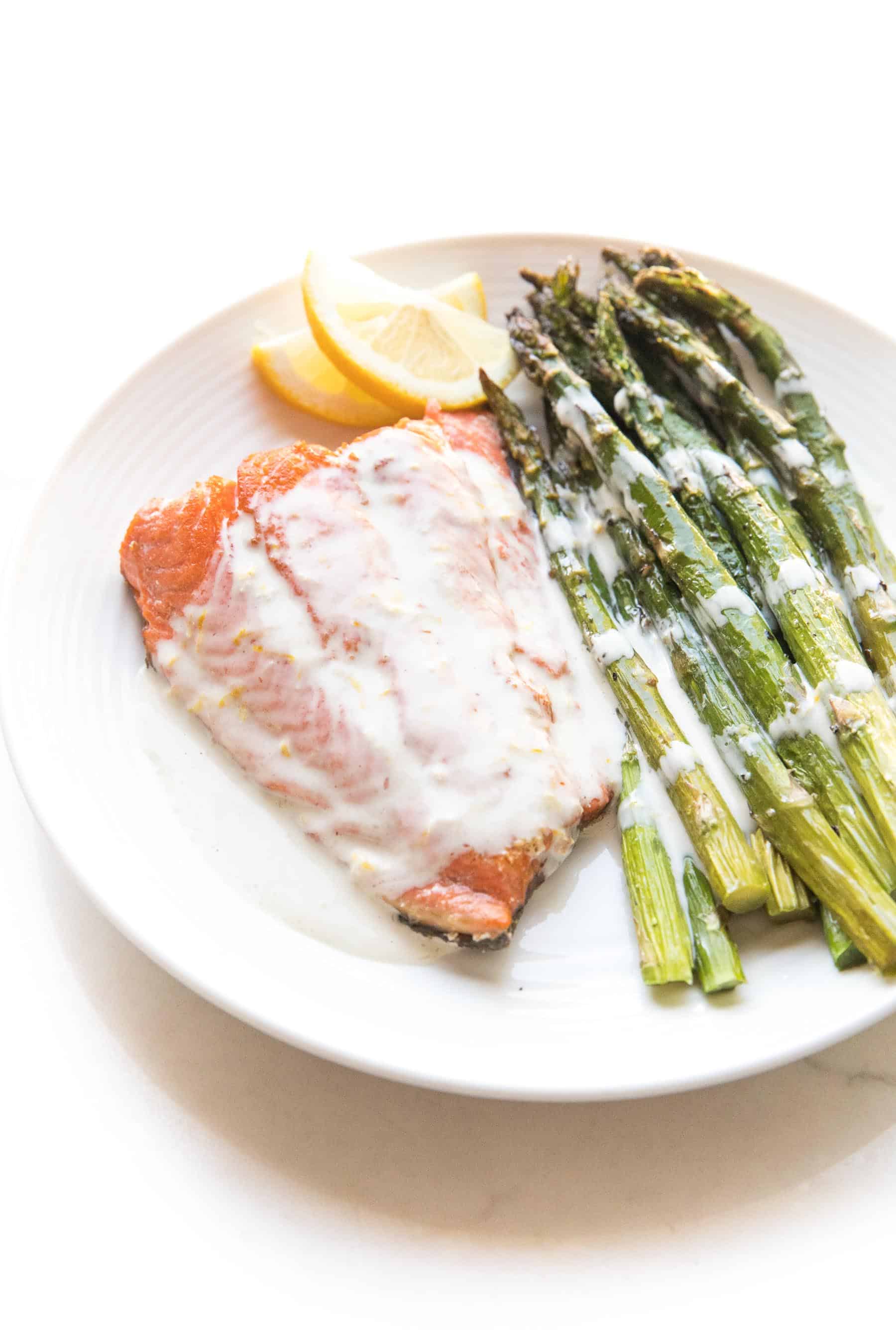 Salmon + asparagus with a white creamy coconut tahini sauce on a white plate and background