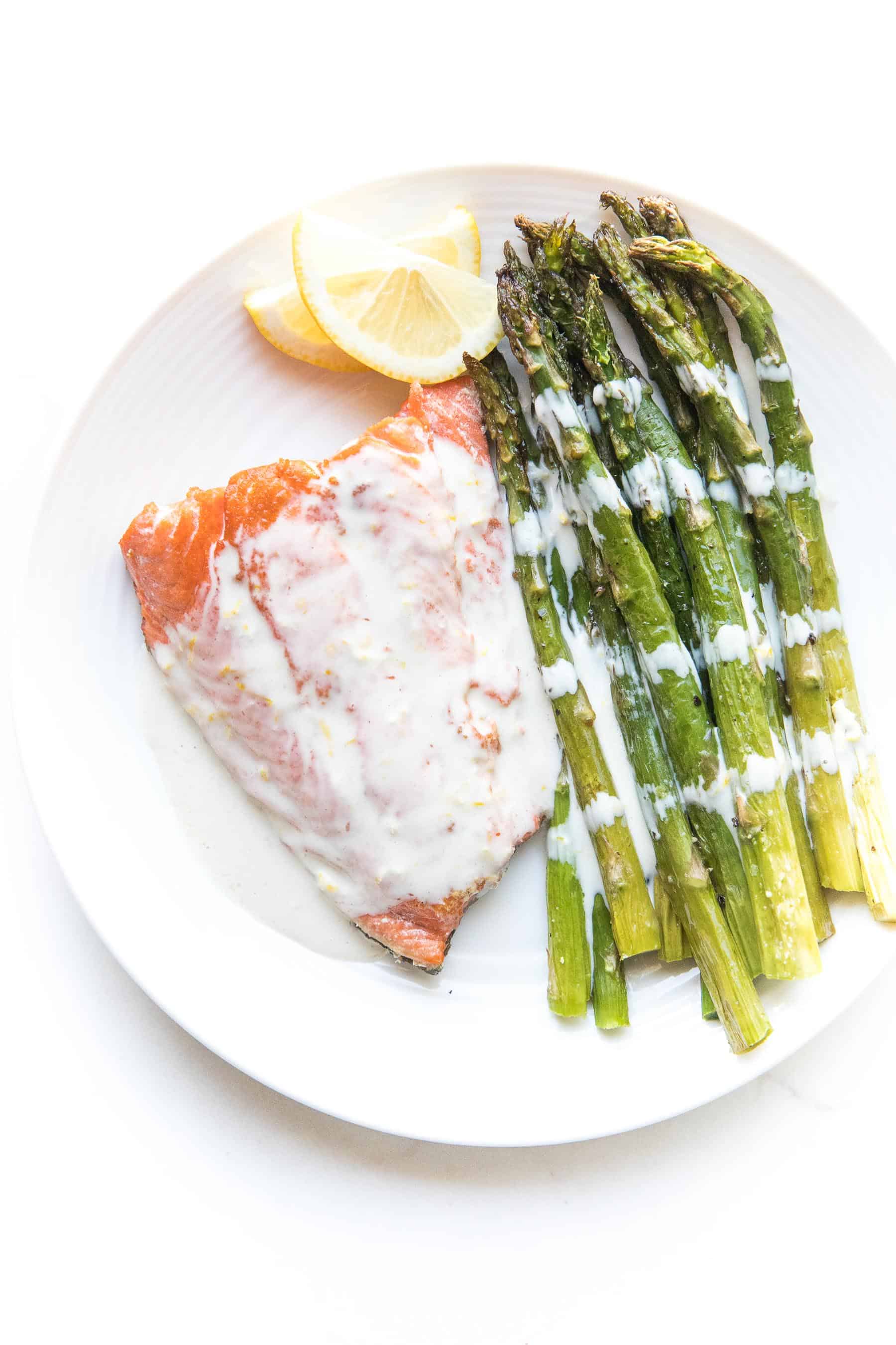 Salmon + asparagus with a white creamy coconut tahini sauce on a white plate and background