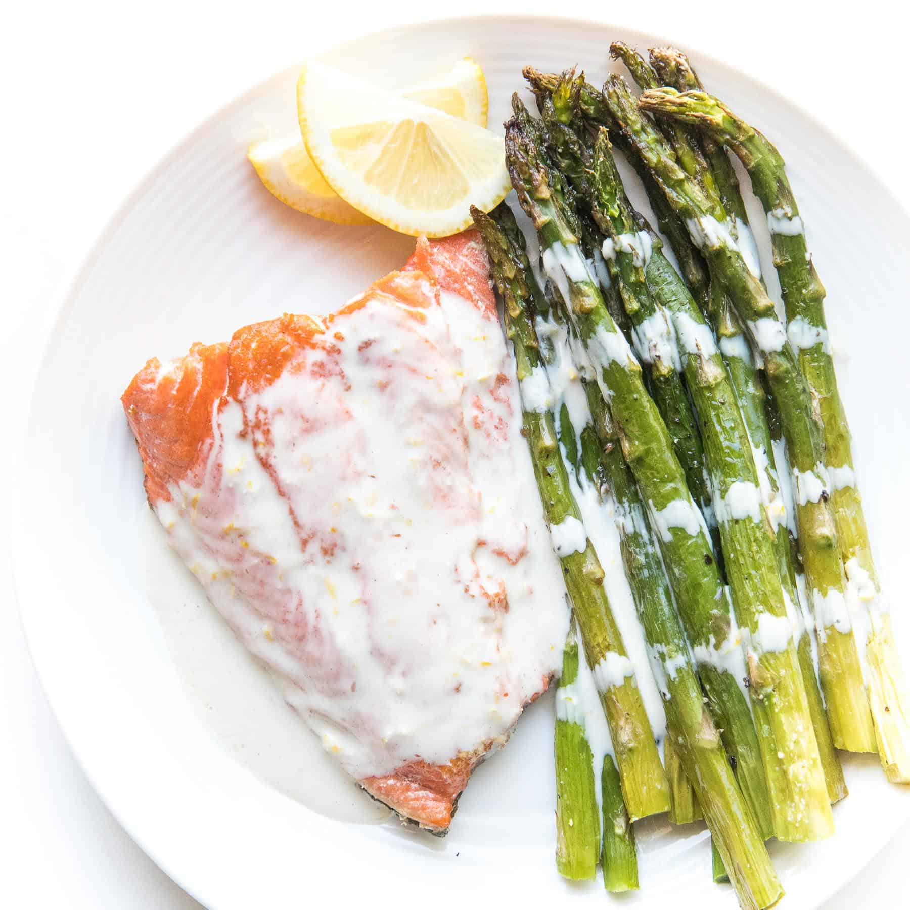 salmon with white sauce with lemon and asparagus on a white plate