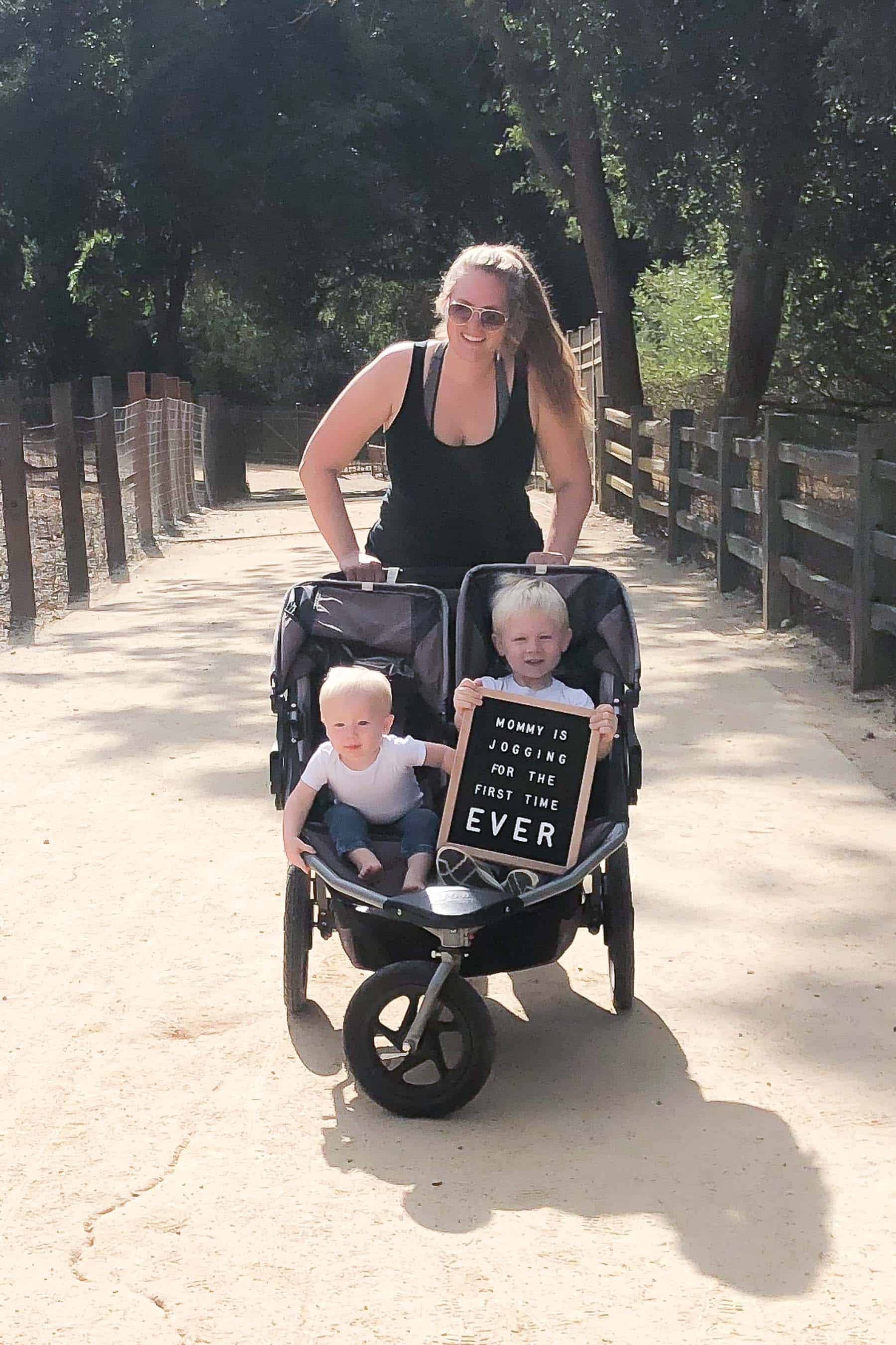 Mom pushing her 2 boys in a double stroller with a letterboard message saying Mommy is jogging for the first time ever