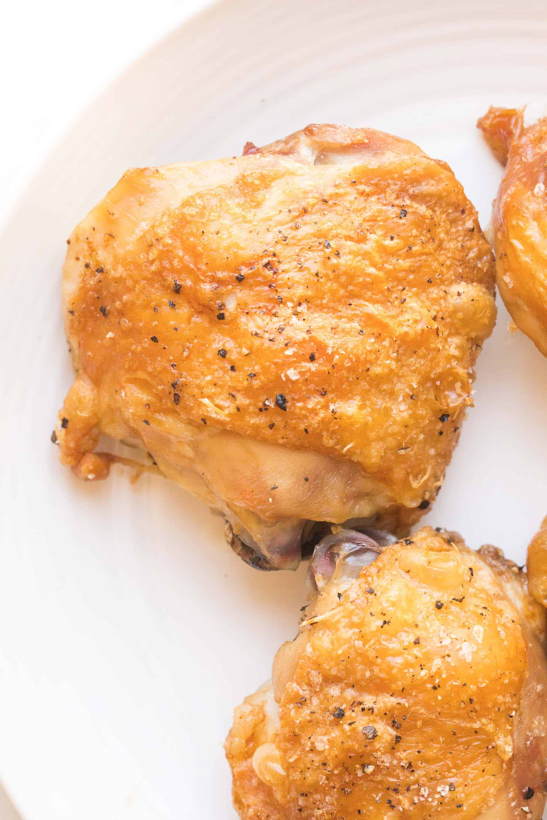 close up of a crispy golden brown chicken thigh on a white plate