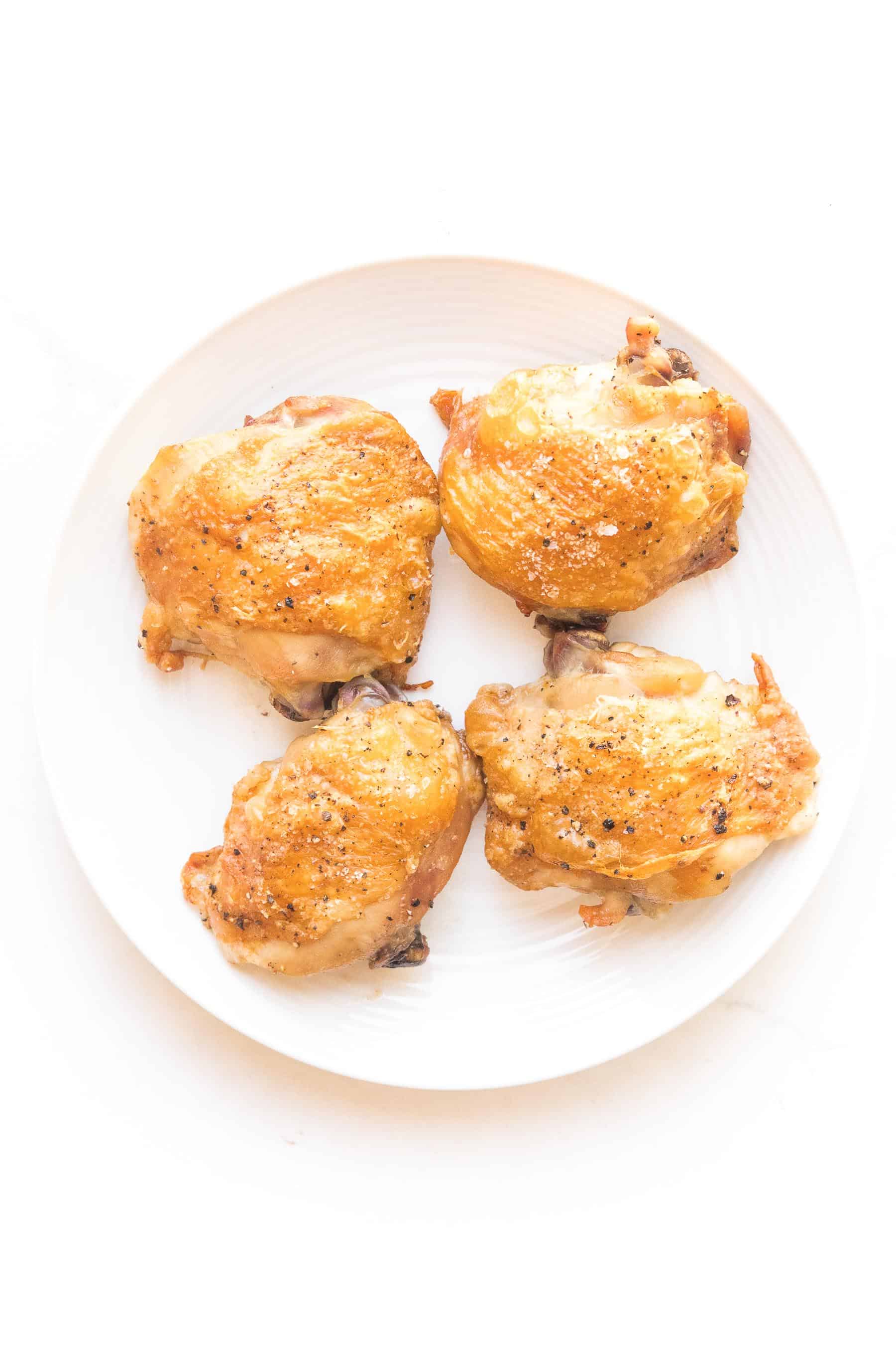 crispy golden brown chicken thighs on a white plate and white background