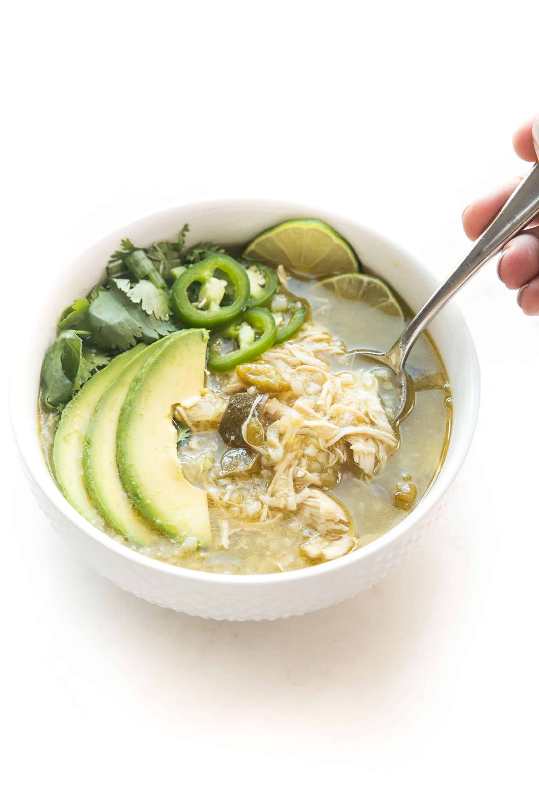 spoon in green verde chicken chili in a white bowl on a white background