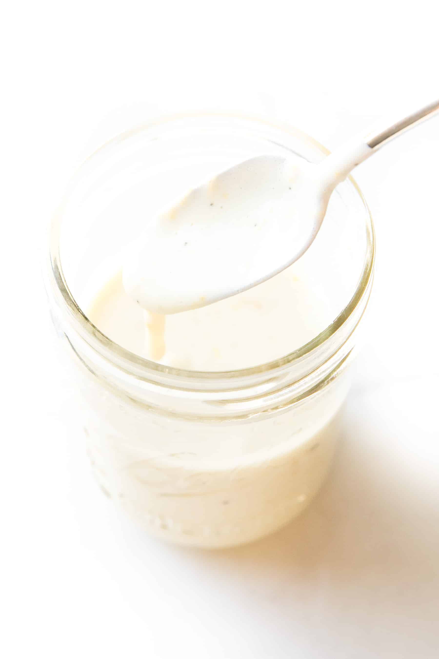 spoon pouring a white lemon garlic aioli sauce into a white mason jar on a white background